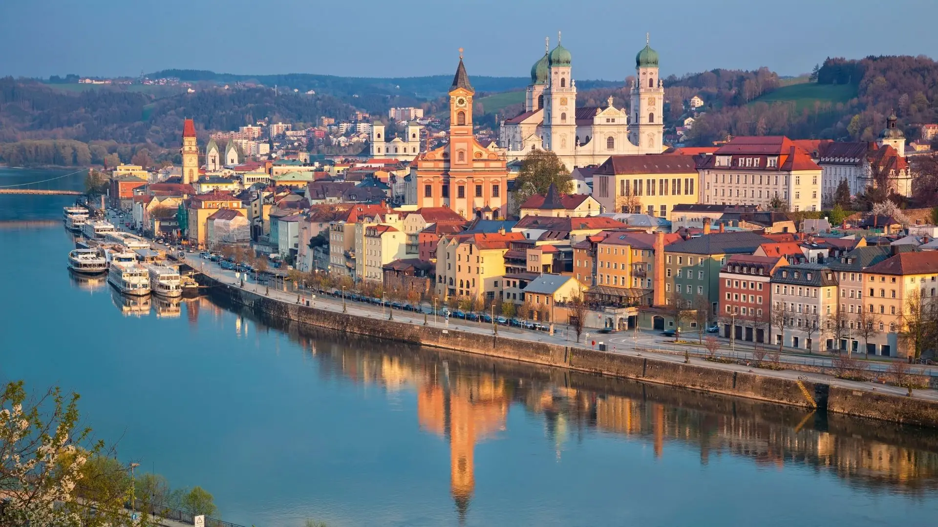 Panoramablick auf die Stadt Passau mit der Donau im Vordergrund, historischen Gebäuden und zwei markanten Türmen im Hintergrund.
