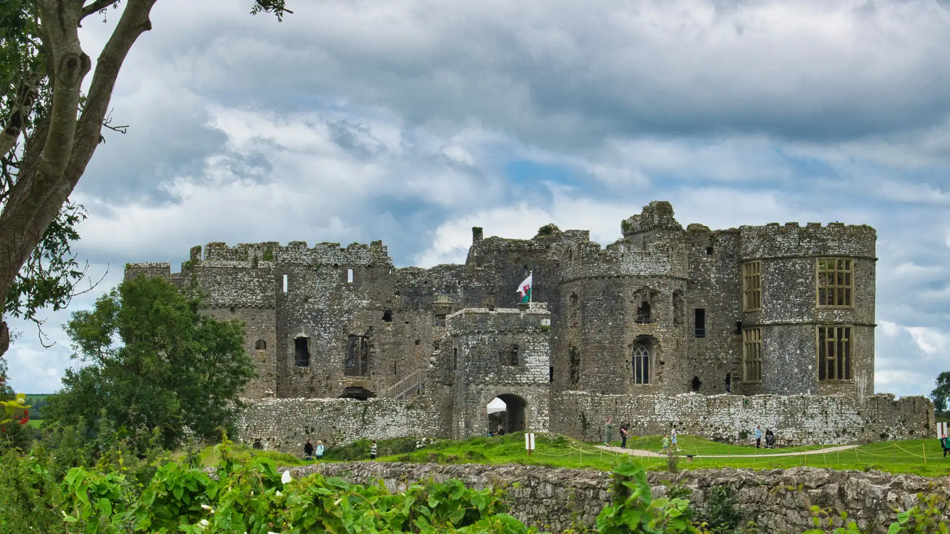 Große mittelalterliche Burg Pembroke aus Stein mit Zinnen und einem Torbogen, umgeben von grüner Wiese und Bäumen unter bewölktem Himmel