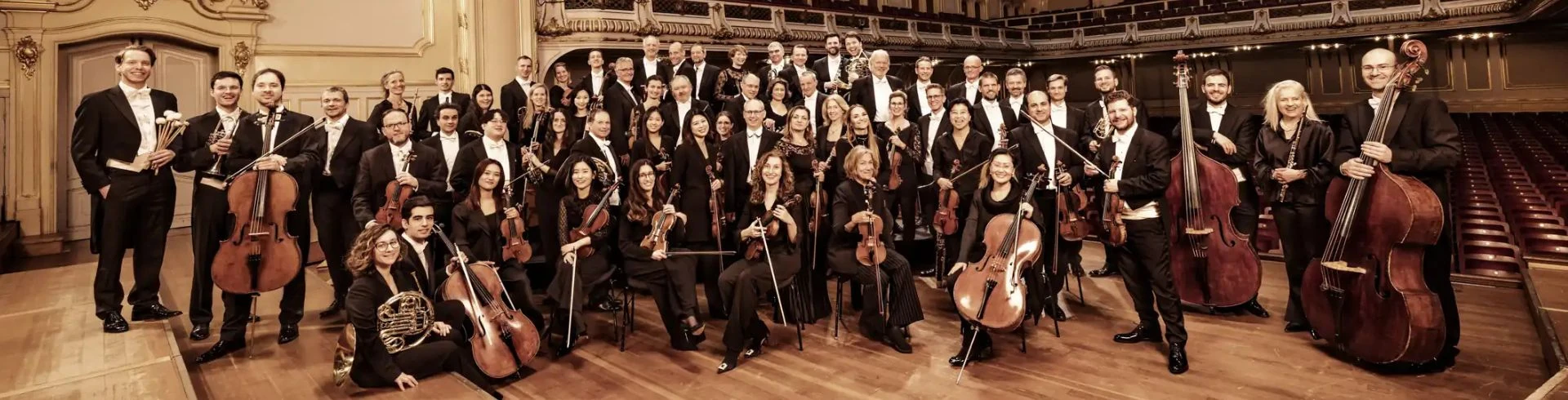Großes Orchester mit Streich-, Holzbläser- und Blechblasinstrumenten auf einer Bühne in einem Konzertsaal