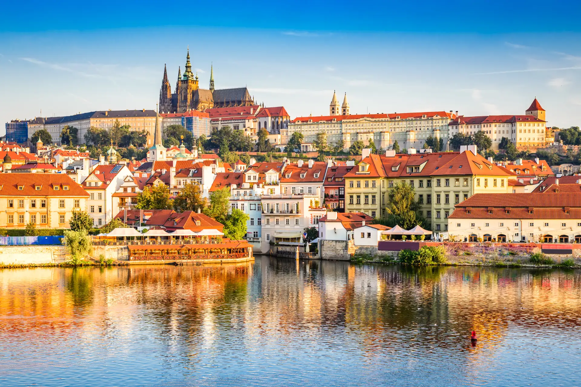 Stadtbild von Prag mit Fluss im Vordergrund und im Sonnenschein zur goldenen Stunde.