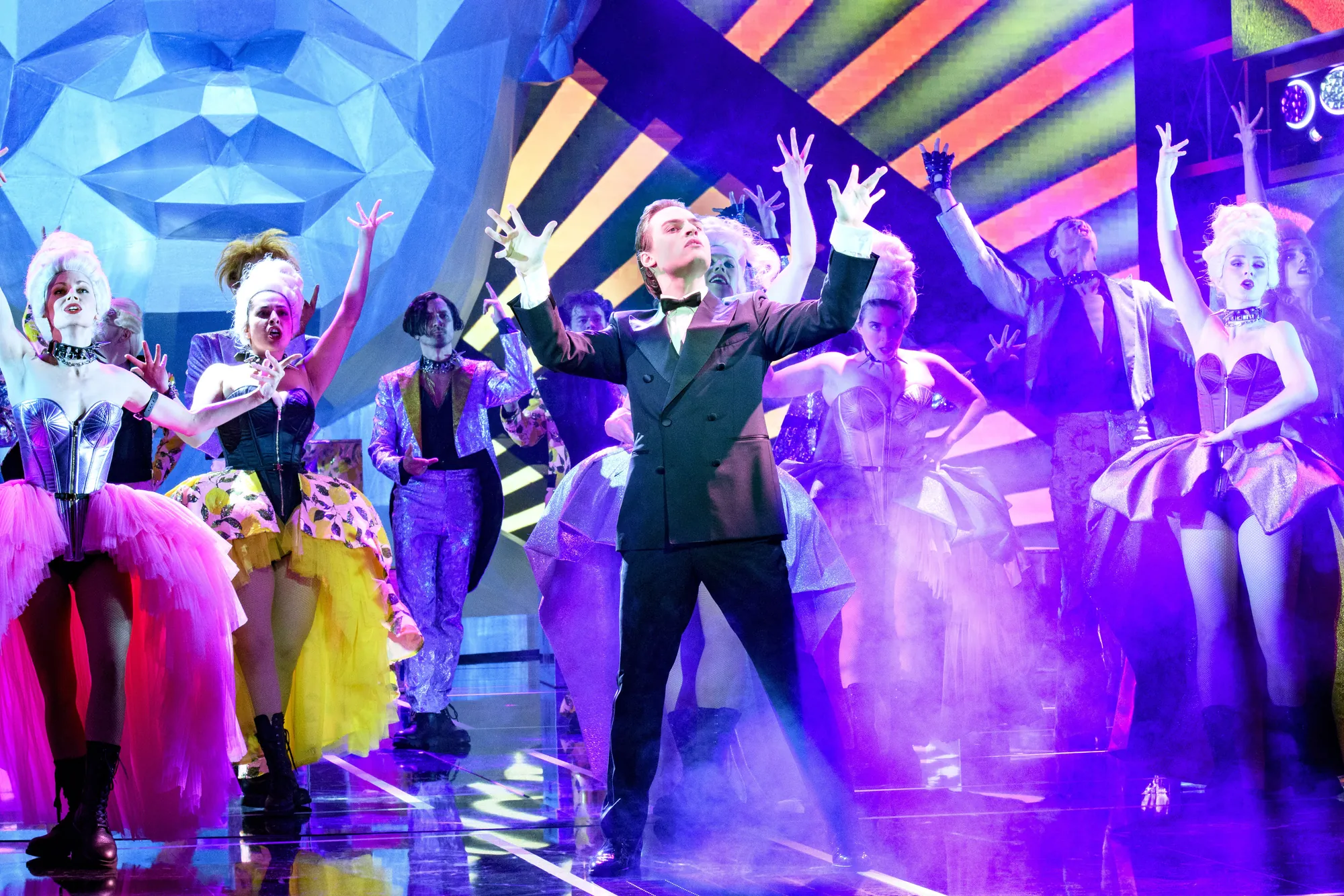 Rock Me Amadeus Musical - Falco auf der Bühne am Präsentieren, umgeben von Menschen in Kostümen