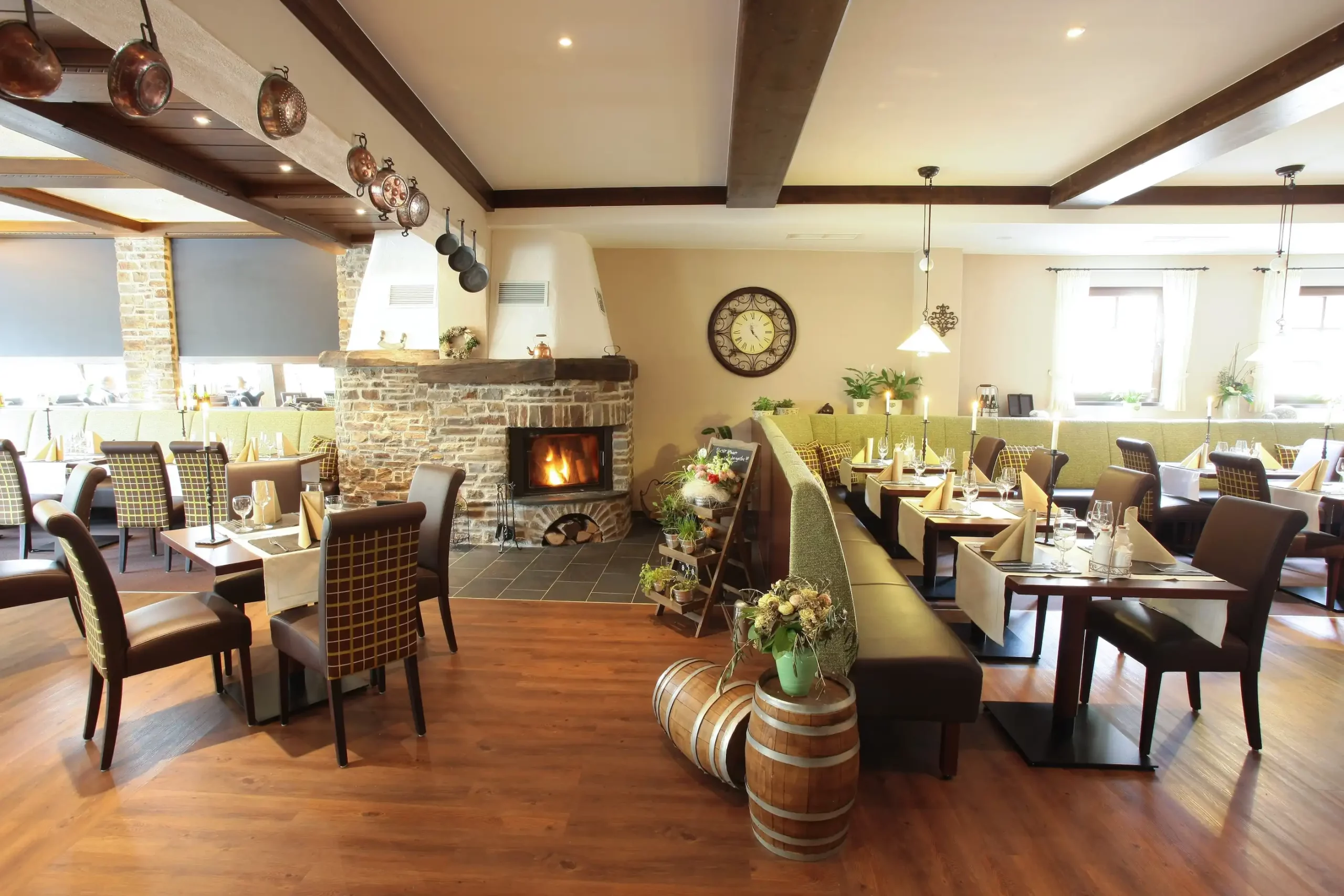 Gemütliches Restaurant mit Holzboden, gemauertem Kamin, Holztischen und Stühlen sowie dekorativen Fässern und Blumenarrangements