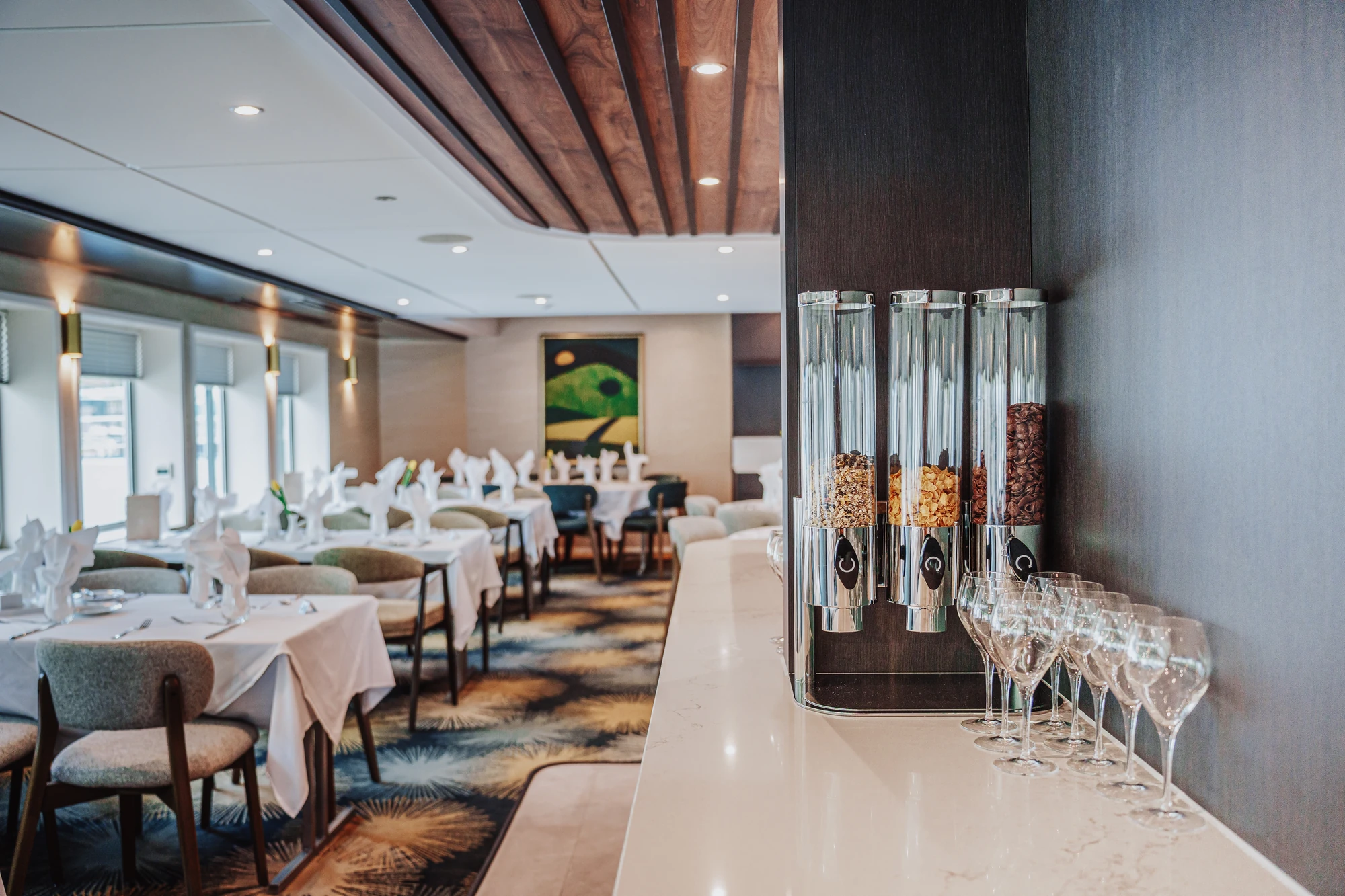 Restaurant mit gedeckten Tischen und Stühlen sowie drei Getreidespendern und Weingläsern auf einer weißen Theke