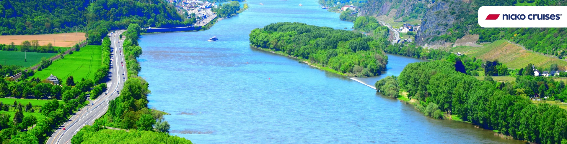 Breiter Fluss mit grünen Uferlandschaften und einer Straße links, aufgenommen während einer Flusskreuzfahrt, Logo von Nicko Cruises oben rechts