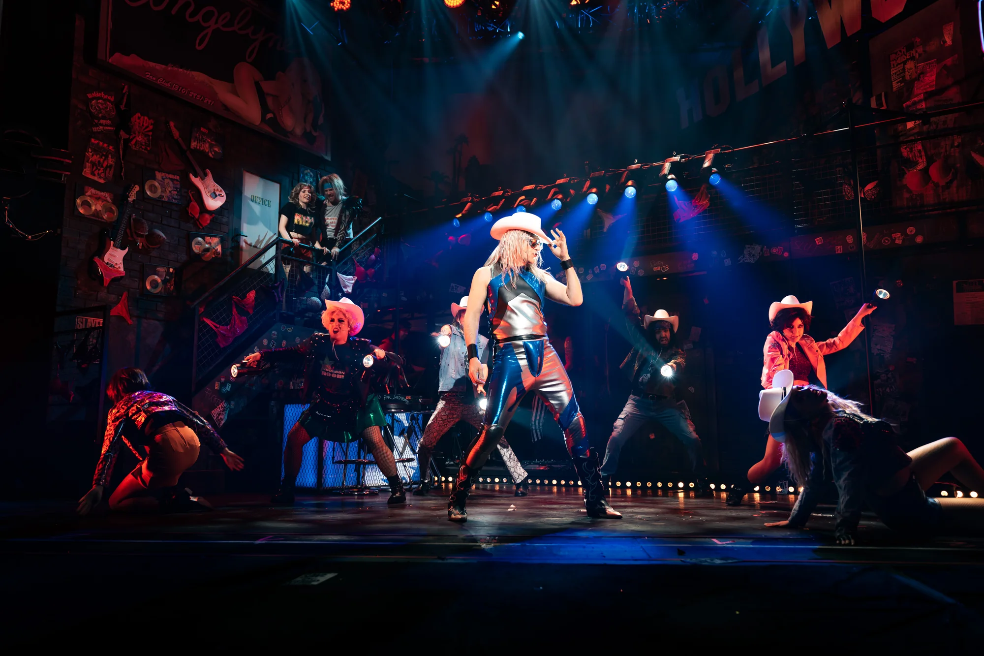Rock of Ages Musical. Mann mit Cowboy Hut und Tänzer mit Taschenlampen