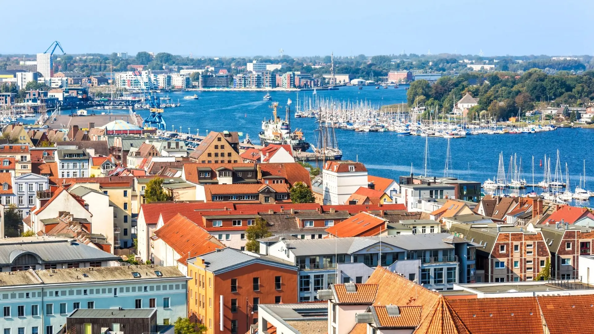 Blick über die Dächer von Rostock zum Hafen mit Segelbooten und der Ostsee im Hintergrund