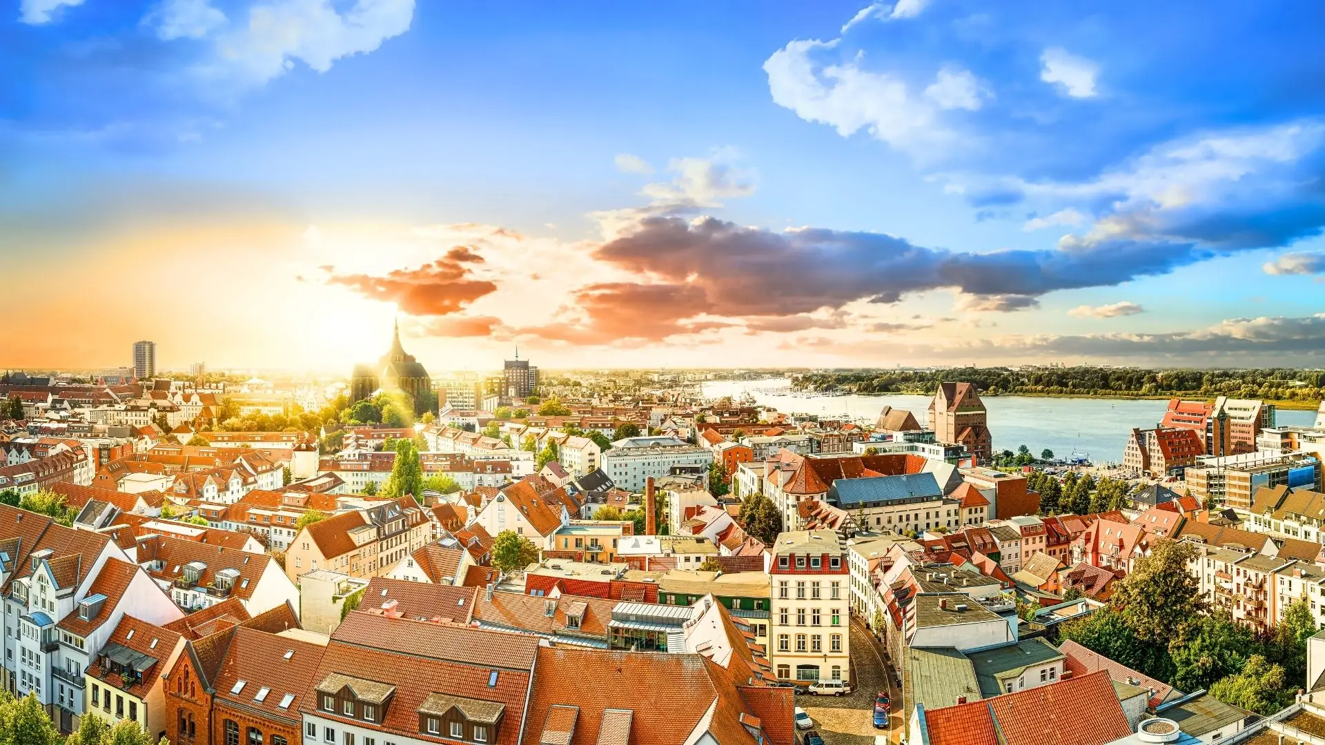 Panorama von Rostock mit historischen Gebäuden, Hafen und Sonnenuntergang am Himmel