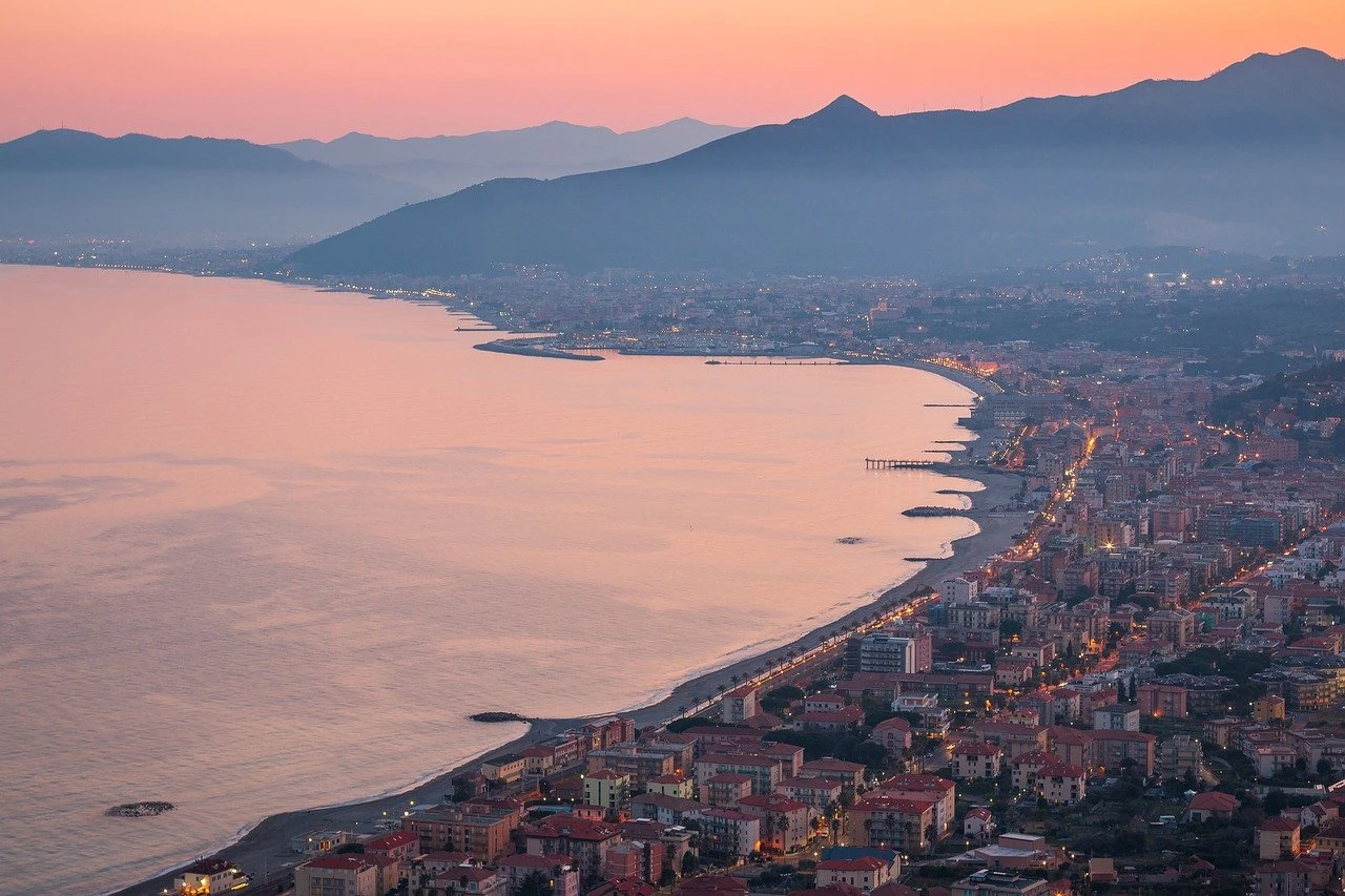 Blick von oben auf eine Stadt am Wasser vor einer Bergkulisse bei Sonnenuntergang