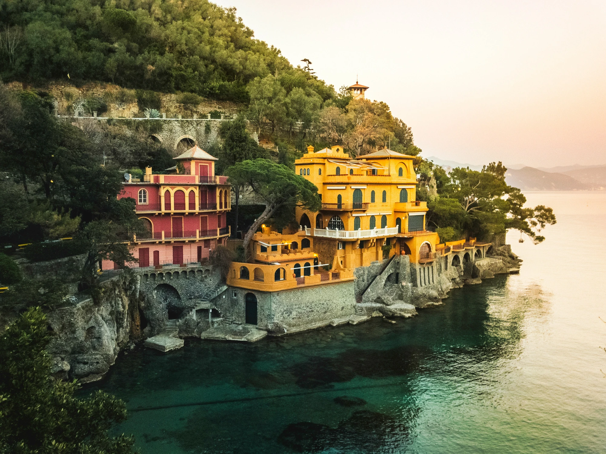 Blick auf eine gelbe und eine rote Villa am Hang am Meer in Italien