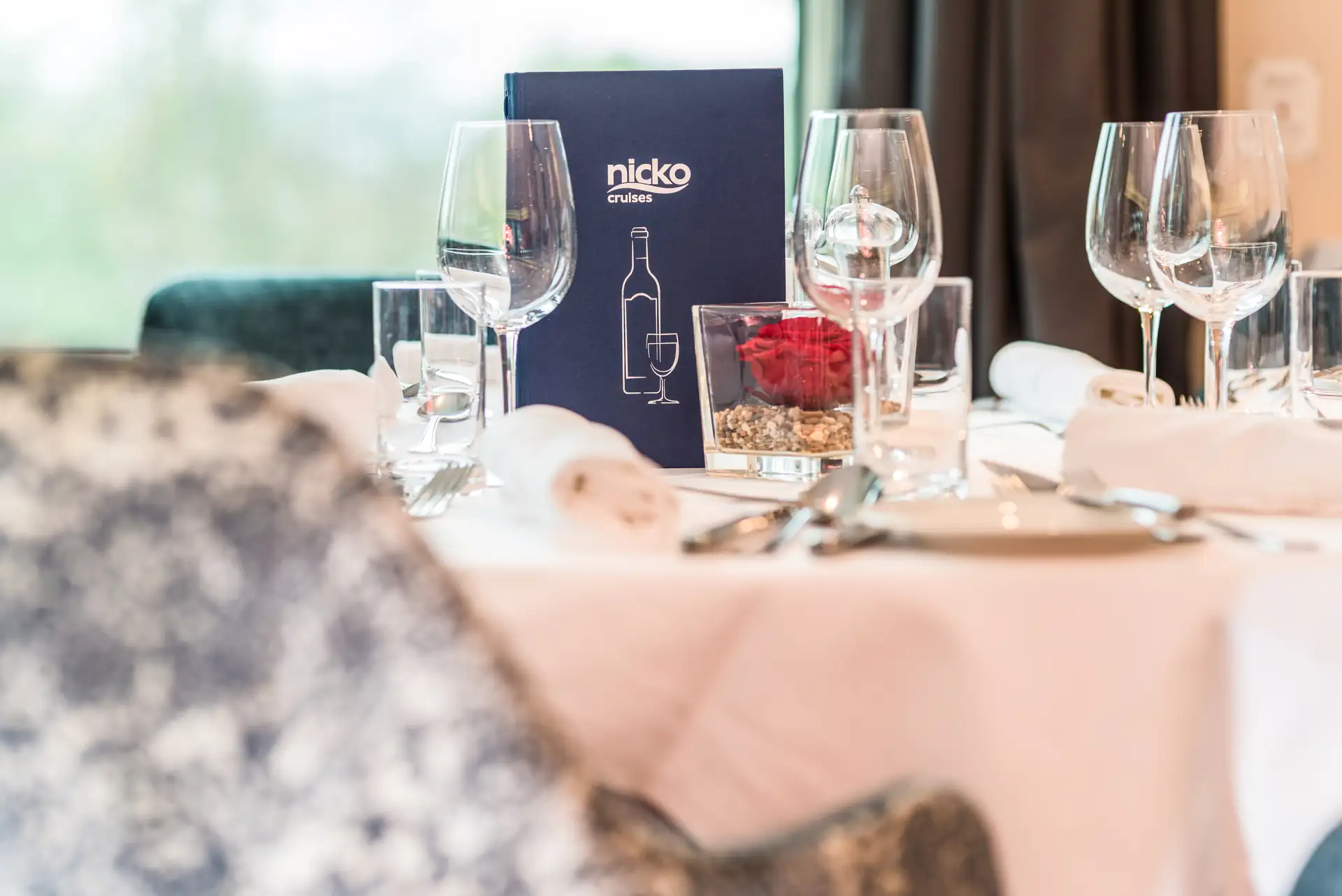 Seine Comtesse Tisch im Restaurant mit weißer Tischdecke, Weingläsern, Wassergläsern, Besteck, Servietten und dunkelblauem Menü mit weißem Schriftzug 'nicko cruises' und Flaschenzeichnung.