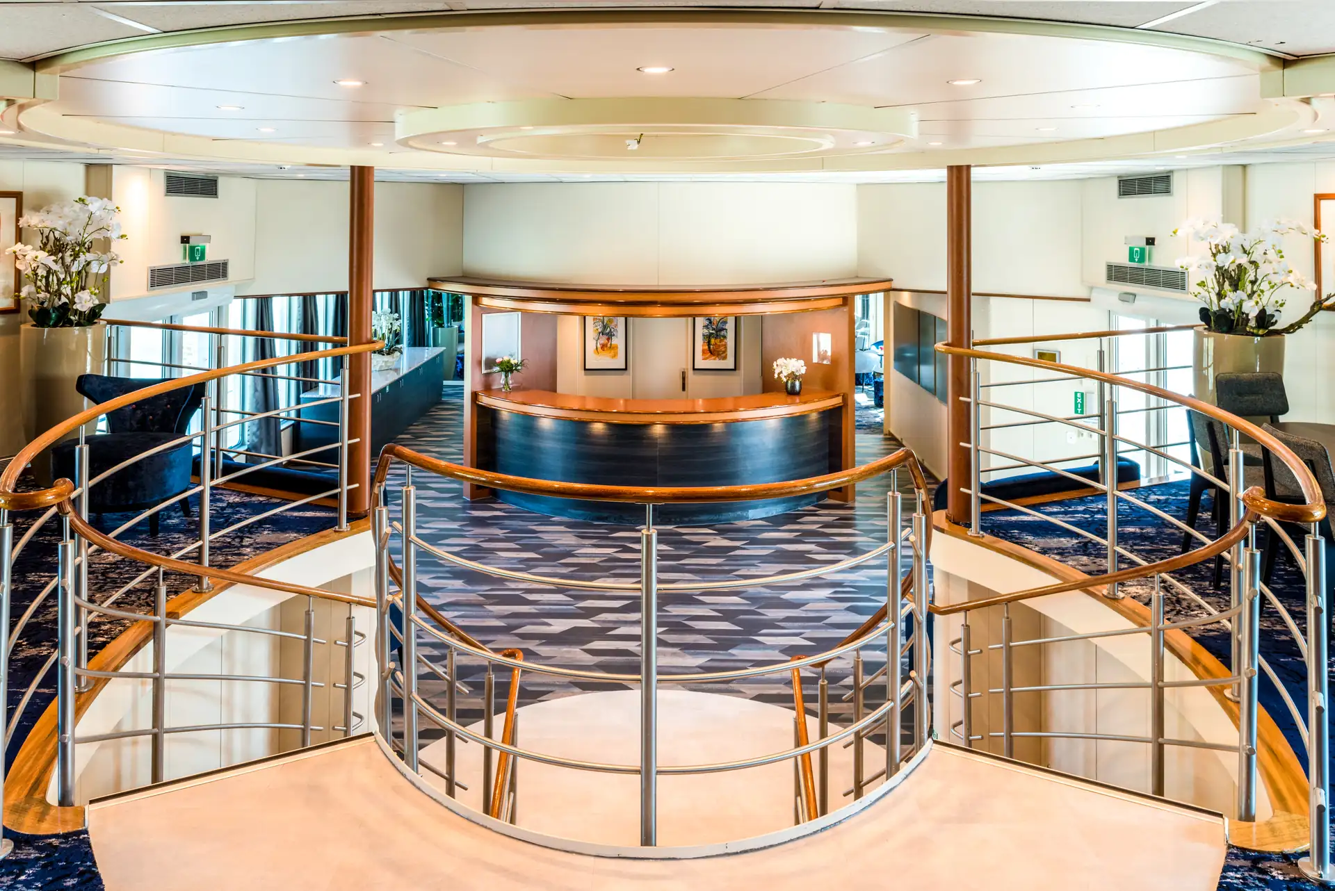 Seine Comtesse Innenraum mit geschwungener Treppe, Holzgeländer und Rezeption mit drei Bildern an der Wand.