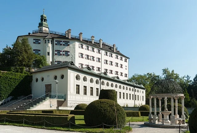 Schloss Ambras in Innsbruck, gesehen aus dem Garten mit gepflegten Grünflächen im Vordergrund.