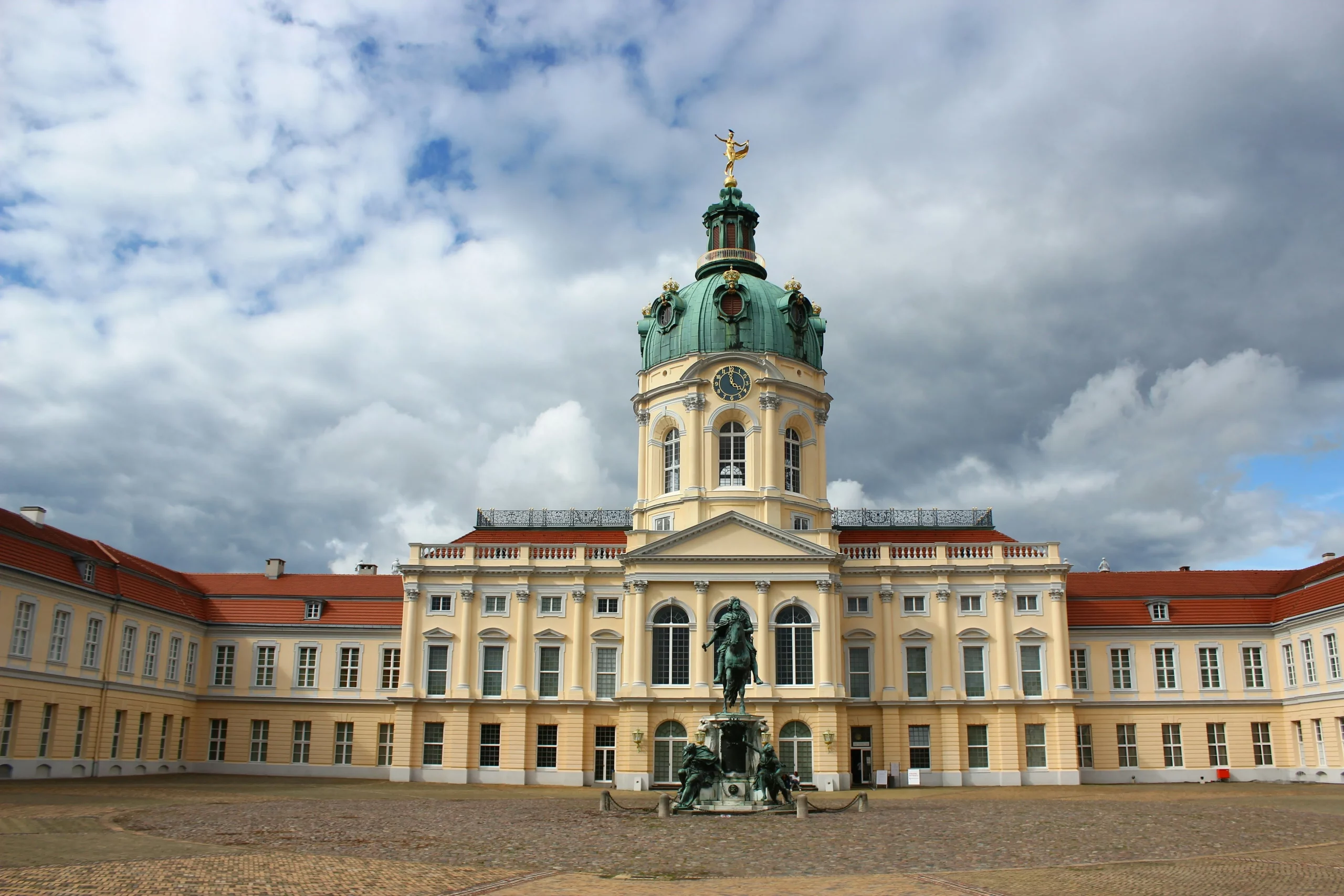 Schloss Charlottenburg mit leerem Vorplatz bei wolkigem Himmel.