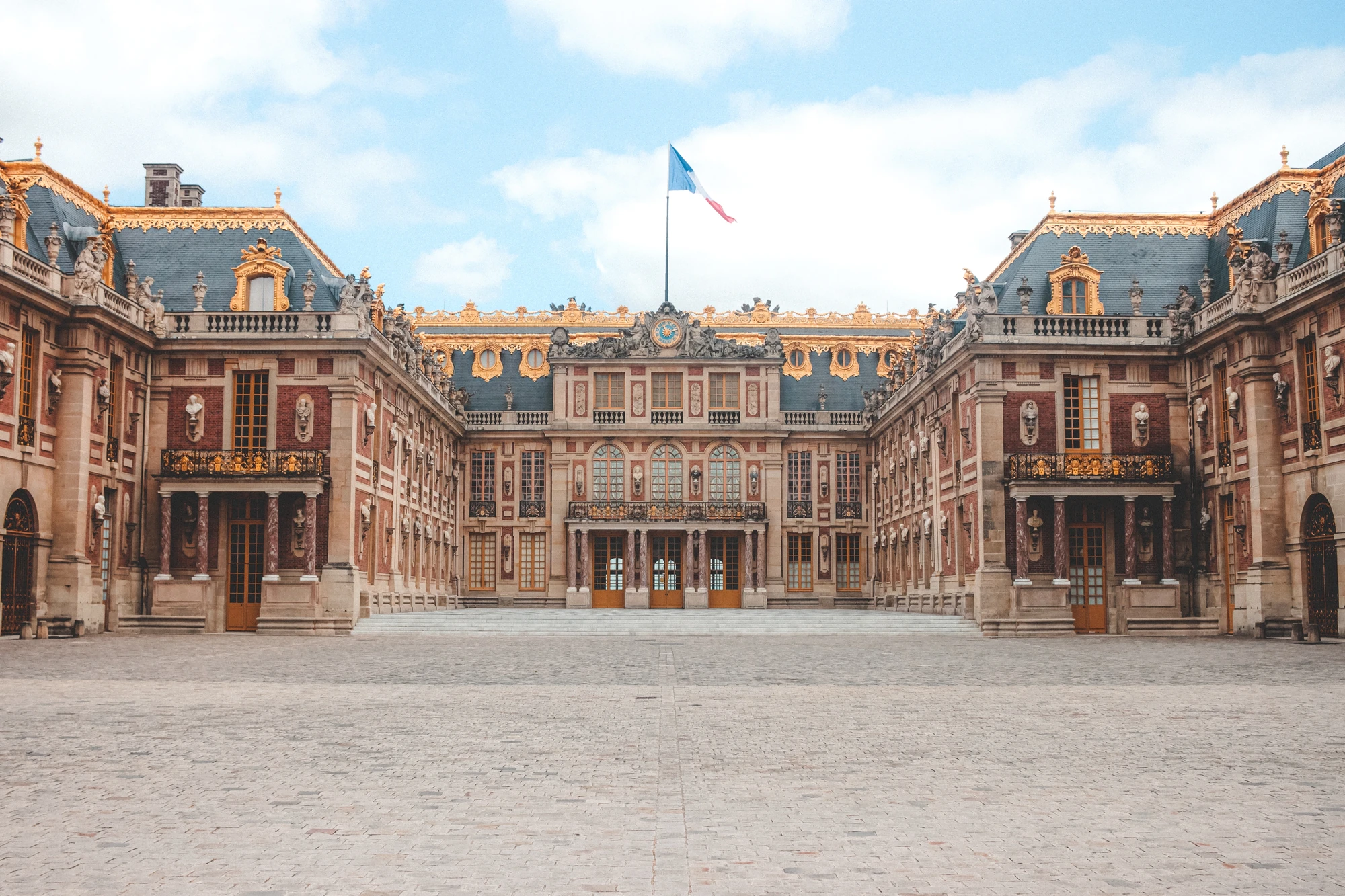 Innenhof des Schlosses Versailles bei Tageslicht, mit prächtigen architektonischen Details und eindrucksvollen Fassaden, die die majestätische Pracht des historischen Gebäudes betonen.