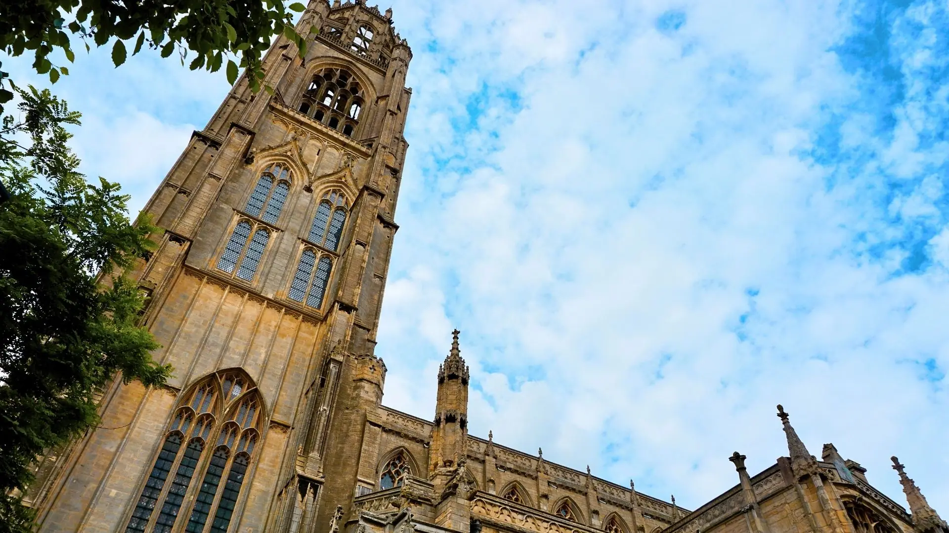 Gotischer Turm der St. Jakobs-Kirche in Rothenburg ob der Tauber vor blauem Himmel mit Wolken.
