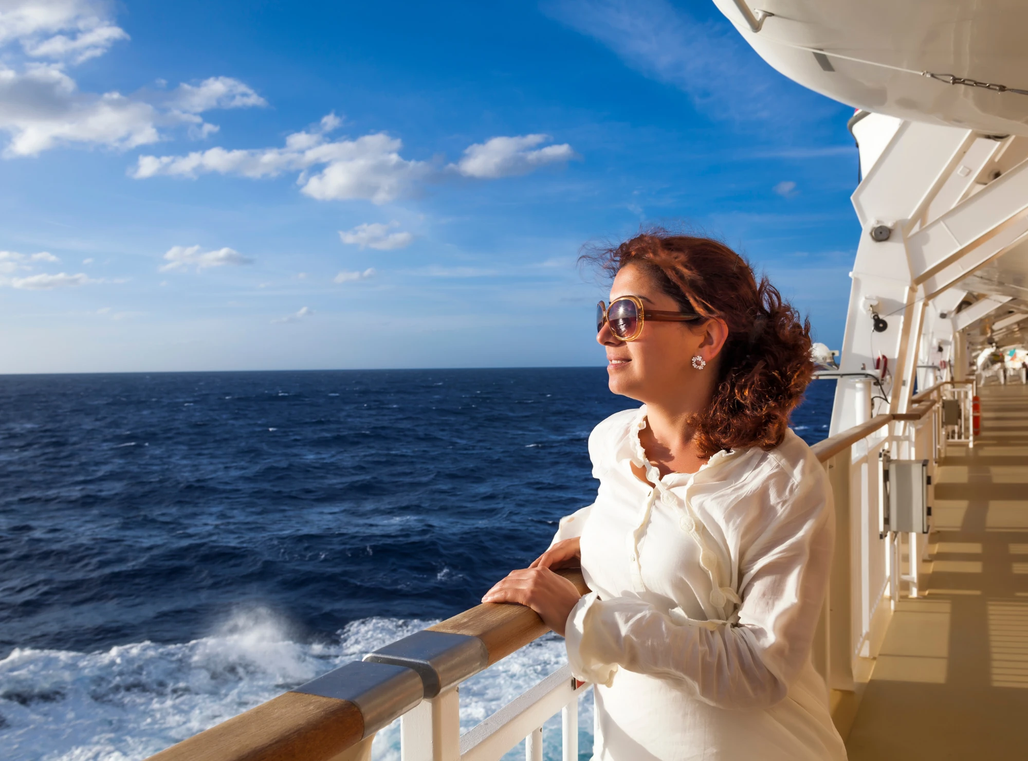 Entspannte Frau auf dem Deck eines Kreuzfahrtschiffs mit Blick auf den Ozean.