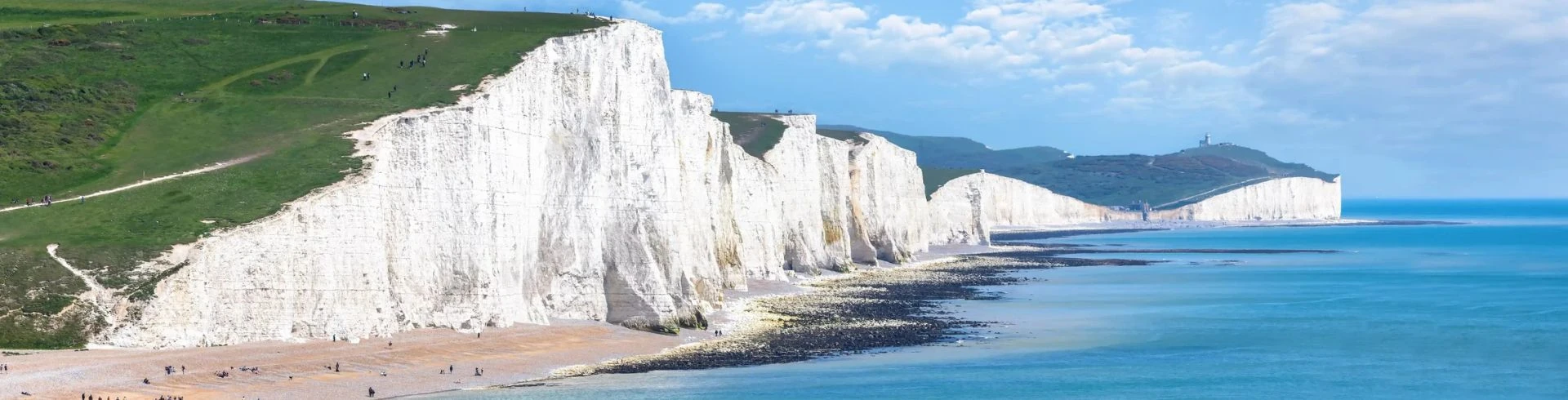 Atemberaubende Kreidefelsen an der Küste mit klarem Wasser und grünem Hügel.