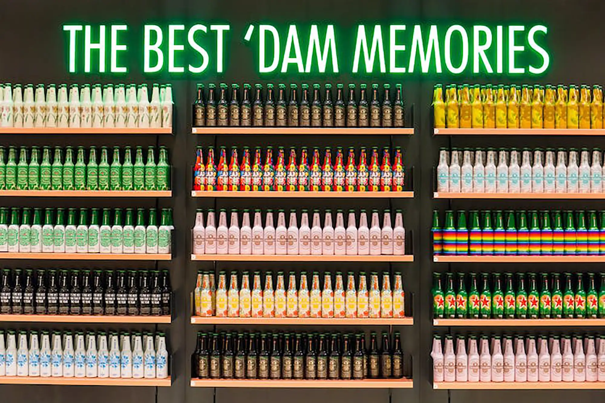Heineken Museum Amsterdam - bunte Bierflaschen auf Regalen an der Wand mit grünem Schriftzug darüber in der Best Dam Bar