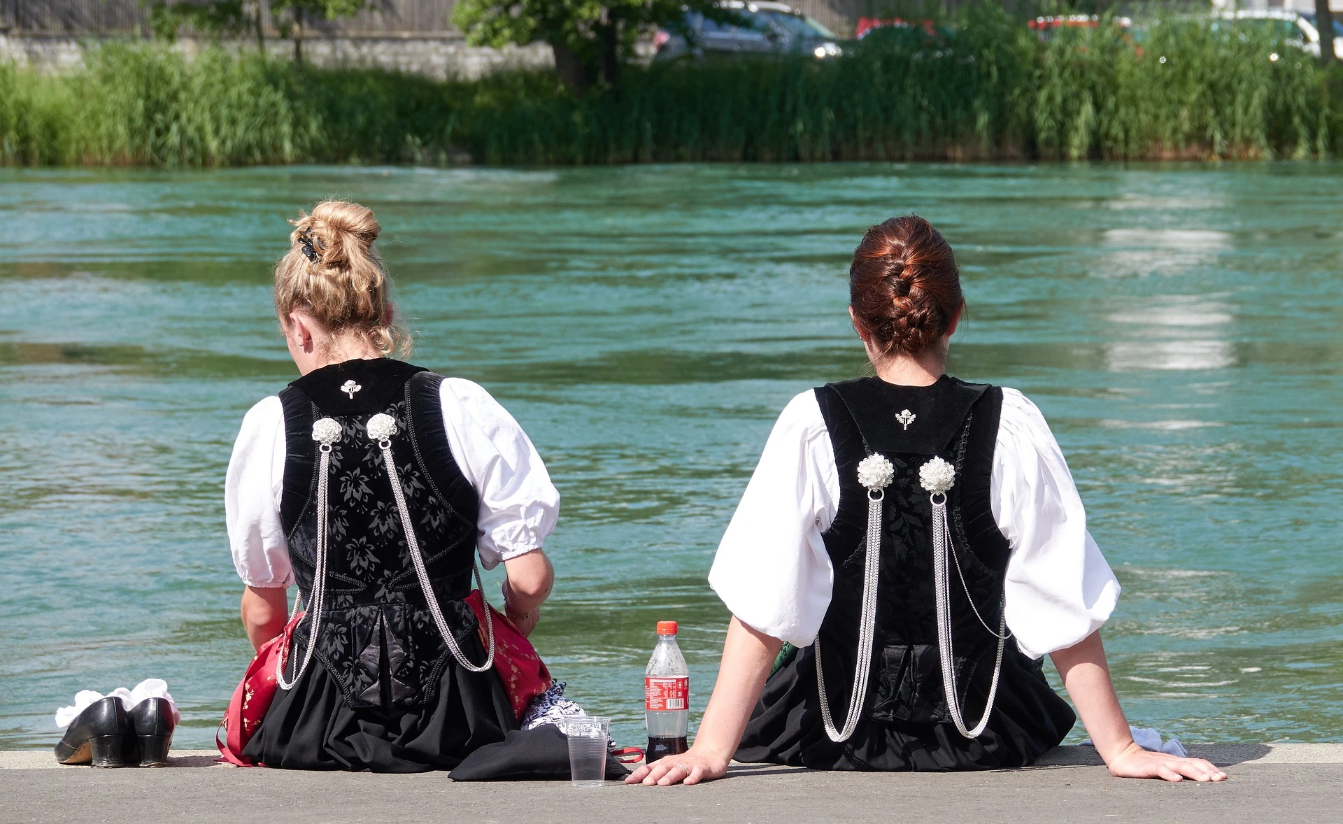 Zwei junge Frauen in Trachten erholen sich bei einer Cola am Ufer des Flusses