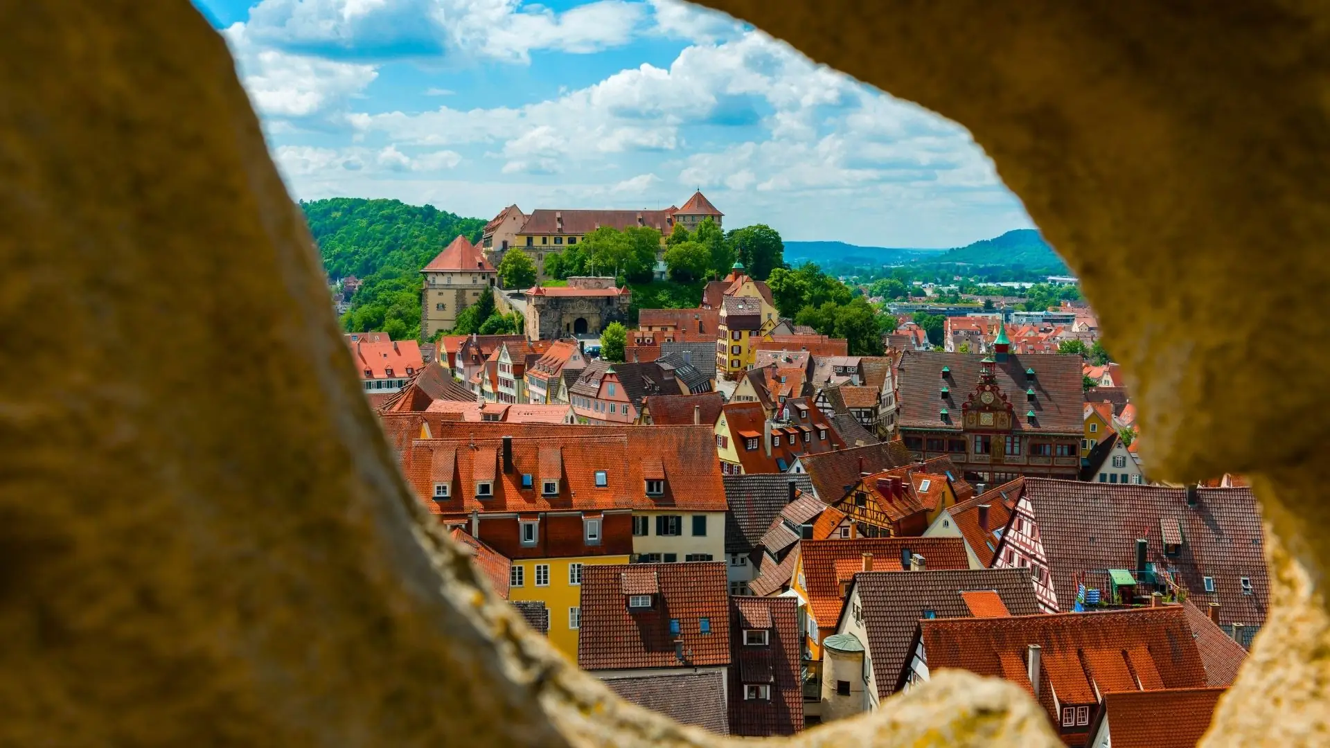 Blick auf die Altstadt von Tübingen mit roten Ziegeldächern und Schloss Hohentübingen im Hintergrund.