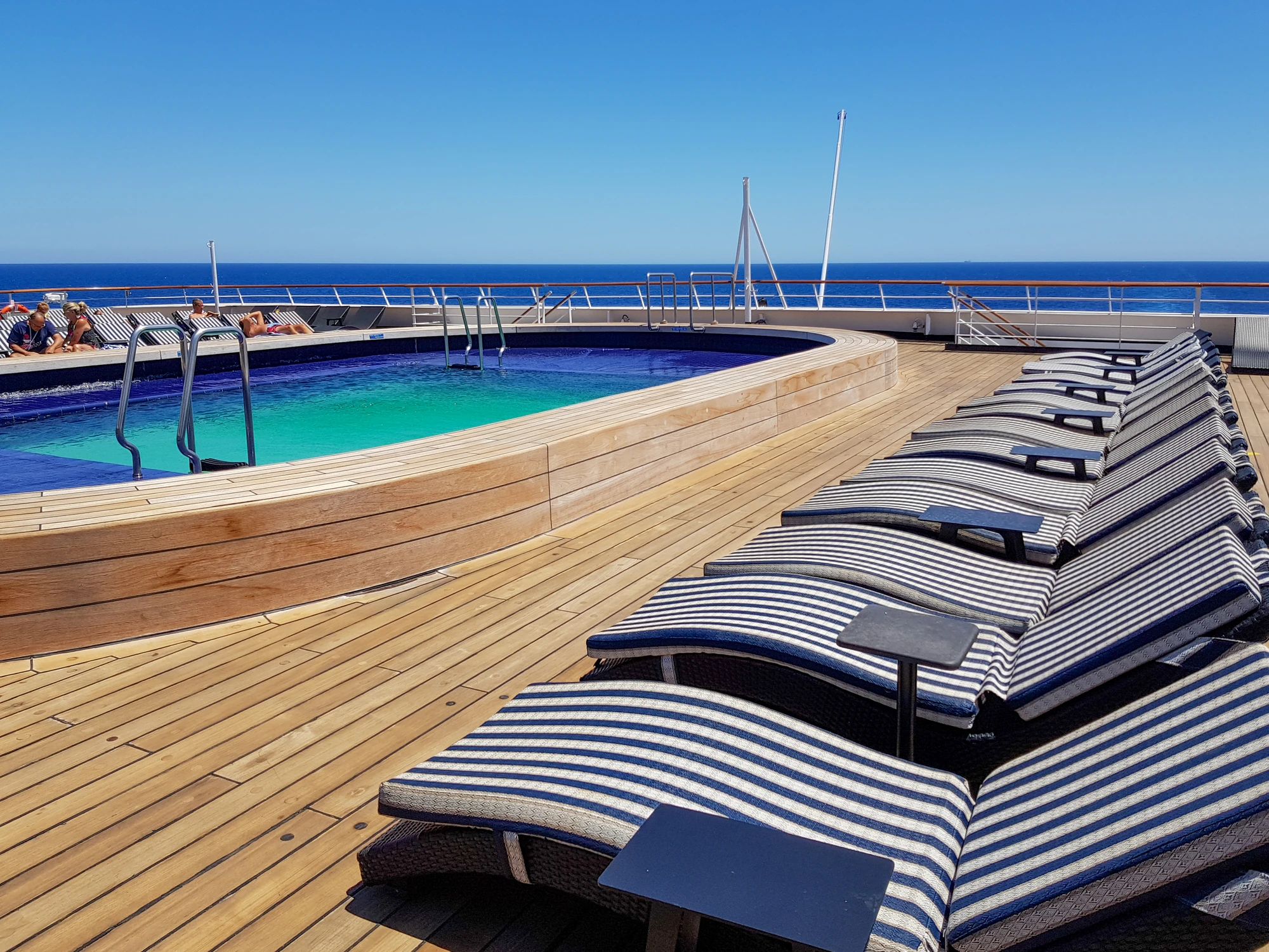 Liegestühle am Pooldeck eines Kreuzfahrtschiffs unter blauem Himmel.
