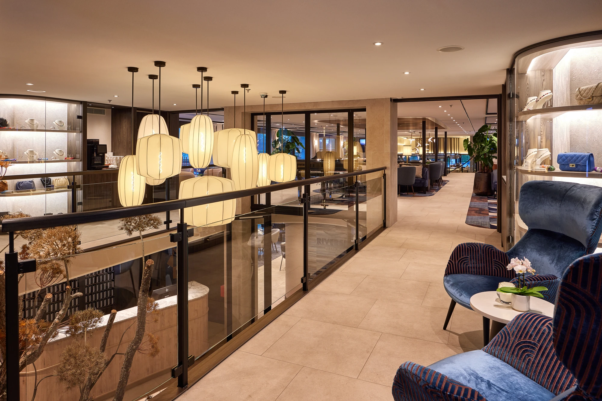 Moderne Lounge mit grauen Sesseln, runden Tischen, einem schwarzen Flügel, Lampen und großen Fenstern mit Blick auf eine Stadt.