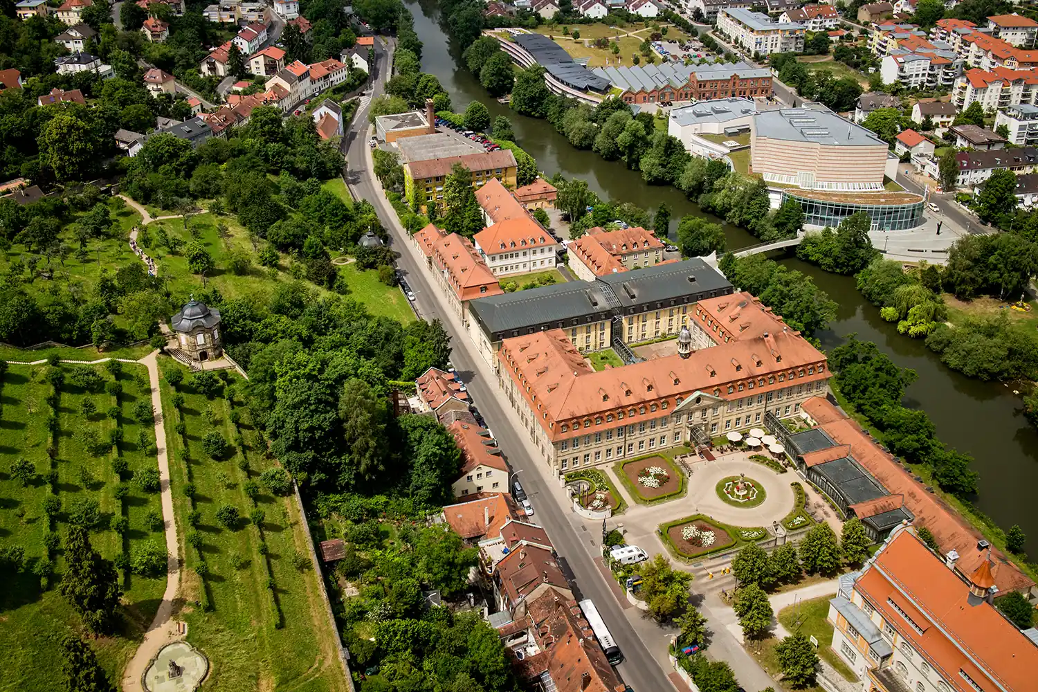 Luftaufnahme des Residenzschlosses Bamberg mit umliegenden Gärten, Straßen und Gebäuden in einer grünen Stadtlandschaft