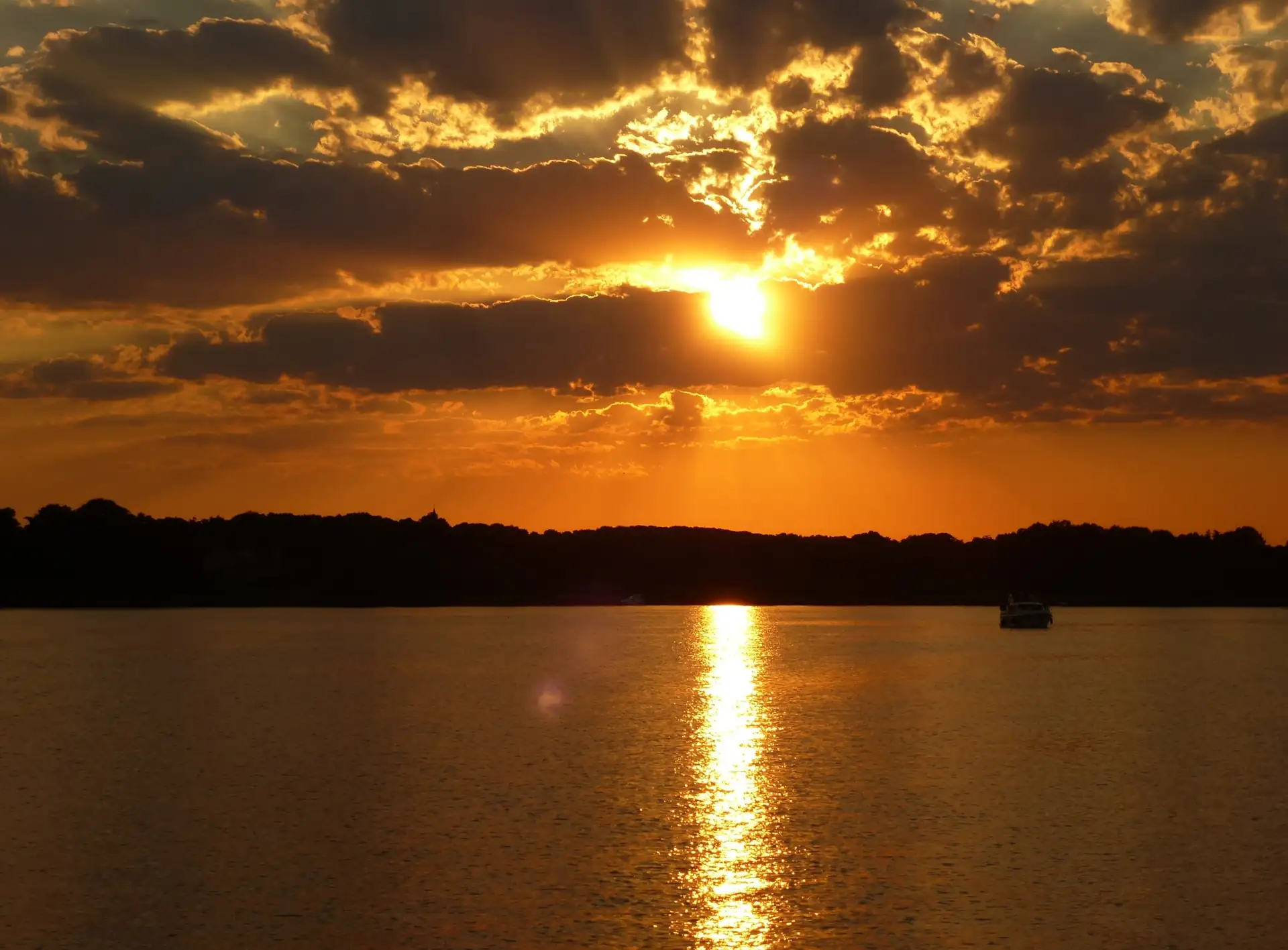 Sonnenuntergang über dem Schwielowsee bei Potsdam mit orangefarbenem Himmel und Sonnenlicht, das sich im Wasser spiegelt
