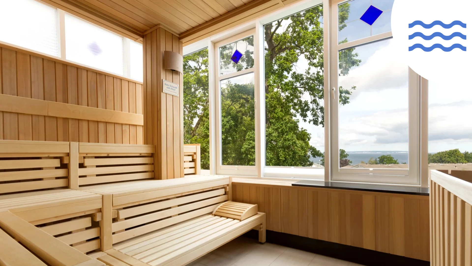 Helle Holzsauna mit Bänken, großen Fenstern mit Blick ins Grüne und auf das Wasser in der Ferne, die ein entspannendes Ambiente schaffen.
