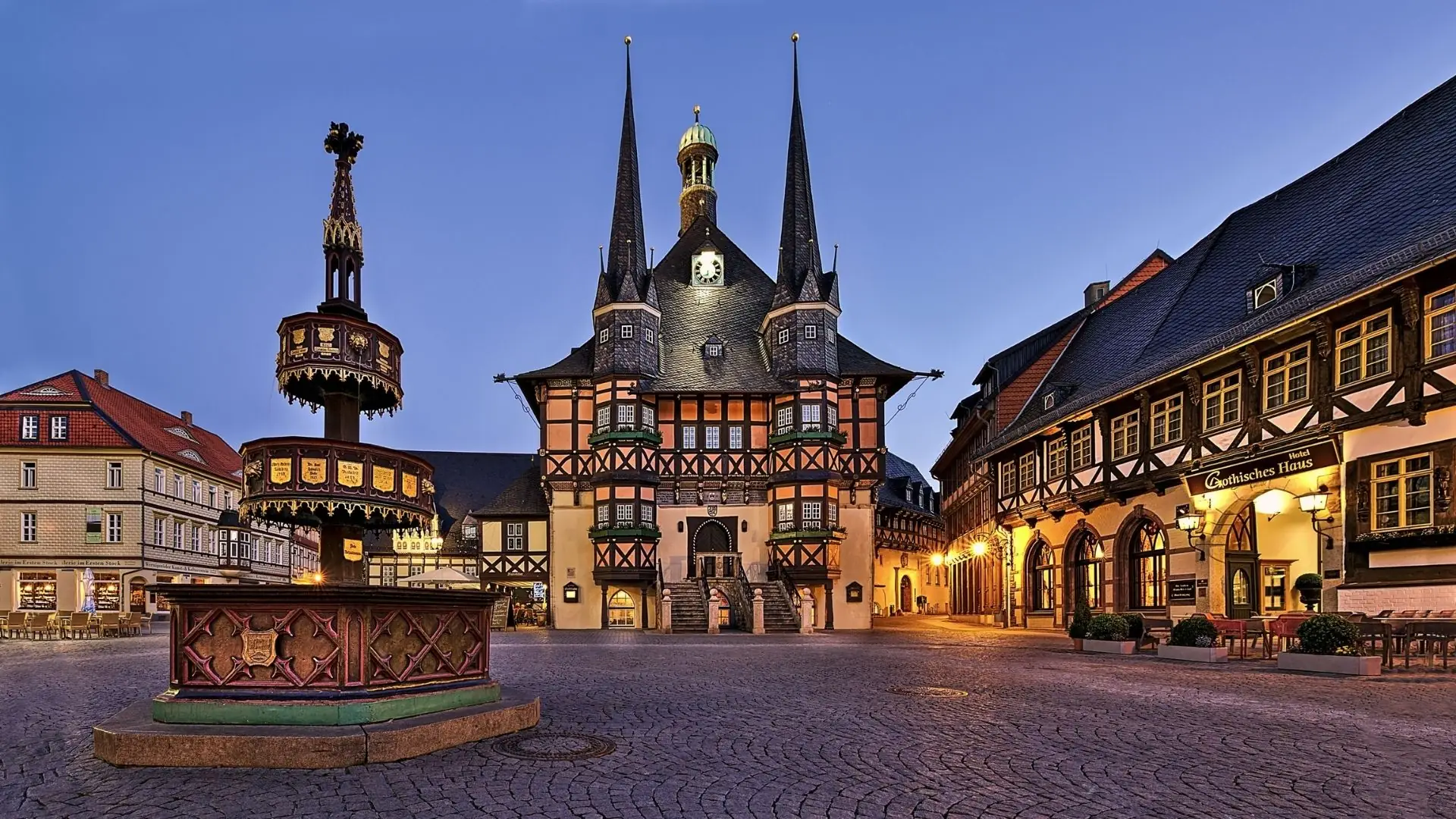 Blick auf das historische Rathaus von Wernigerode mit drei spitzen Türmen, umgeben von Fachwerkhäusern und einem Brunnen im Vordergrund.