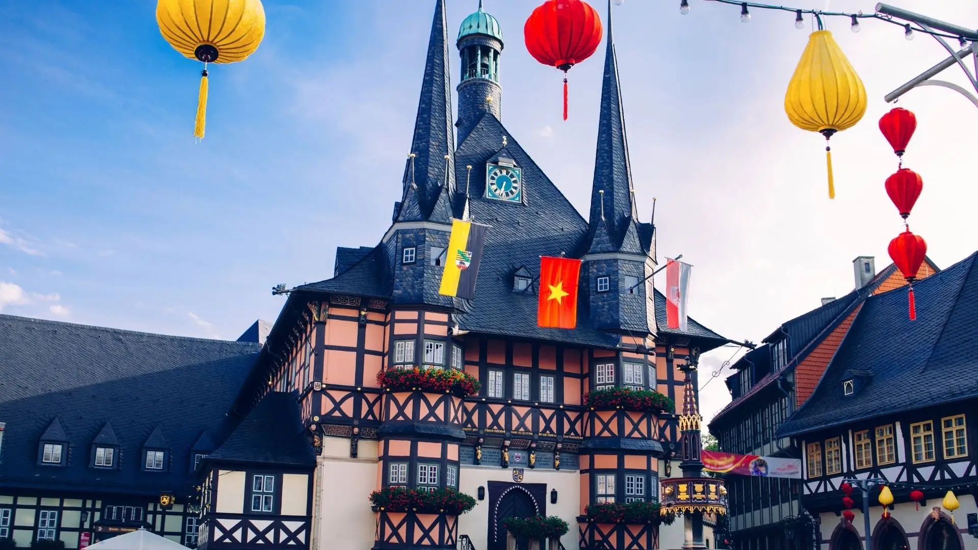 Das historische Rathaus von Wernigerode mit drei spitzen Türmen, umgeben von bunten Laternen. An der Fassade hängen Blumenkästen.