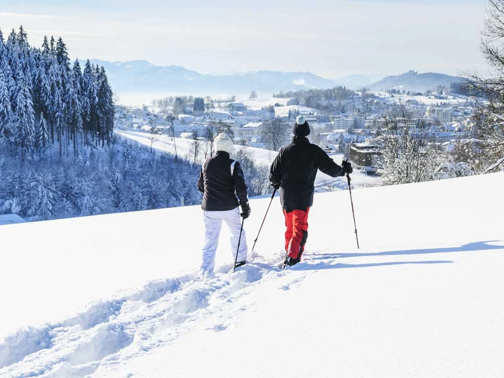 Zwei Personen beim Winterwandern in einer sonnigen Atmosphäre mit Blick auf eine Stadt