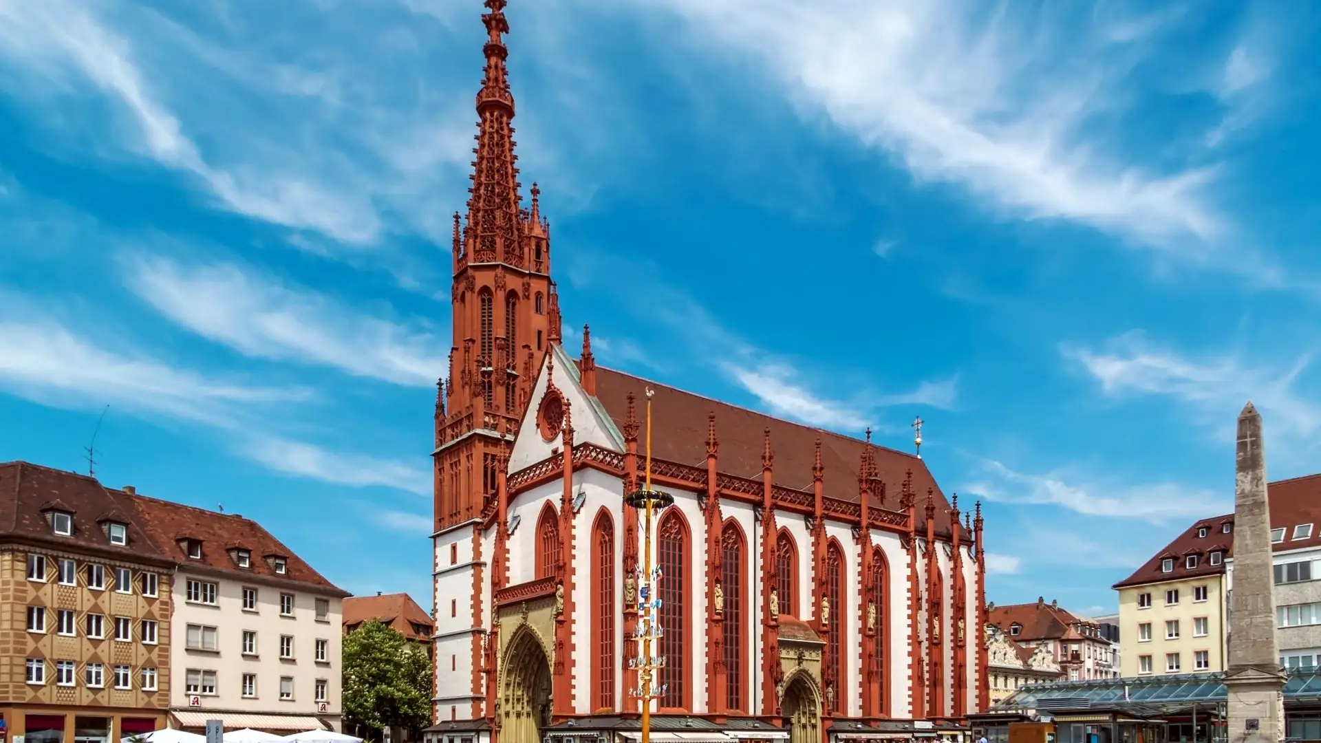Gotische Fassade und hoher Turm des Würzburger Doms vor blauem Himmel, umgeben von historischen Gebäuden.