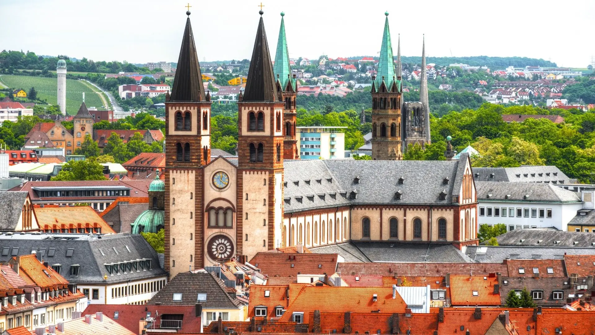 Würzburger Dom mit seinen vier markanten Türmen, umgeben von roten Dächern und grünen Hügeln im Hintergrund