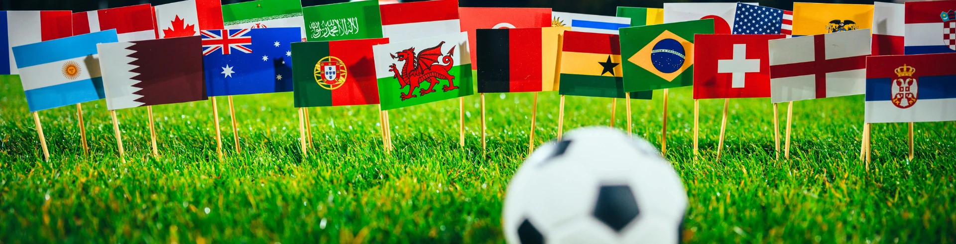 Fußball auf Gras vor einer Reihe von kleinen Nationalflaggen verschiedener Länder