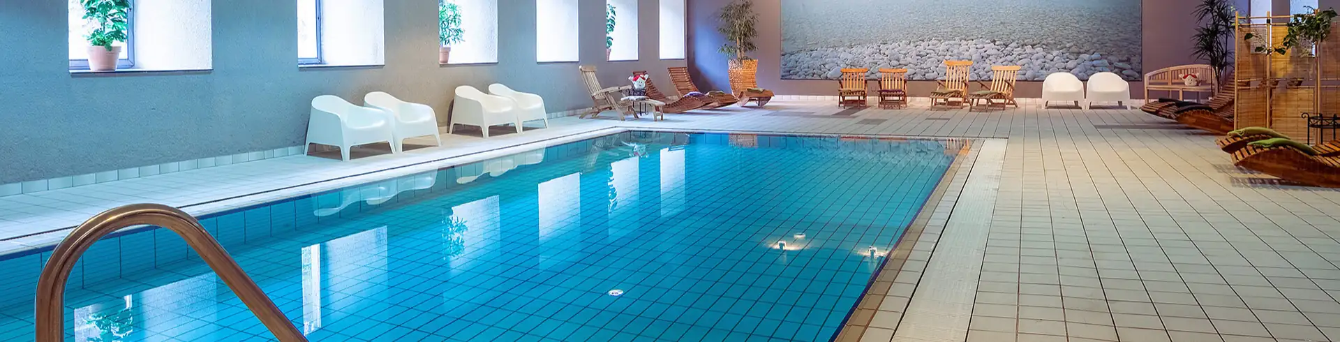 Bild im Bannerformat: Wellnessbereich im Achat Hotel Monschau mit rechteckigem Schwimmbecken, Liegestühlen und großen Fenstern