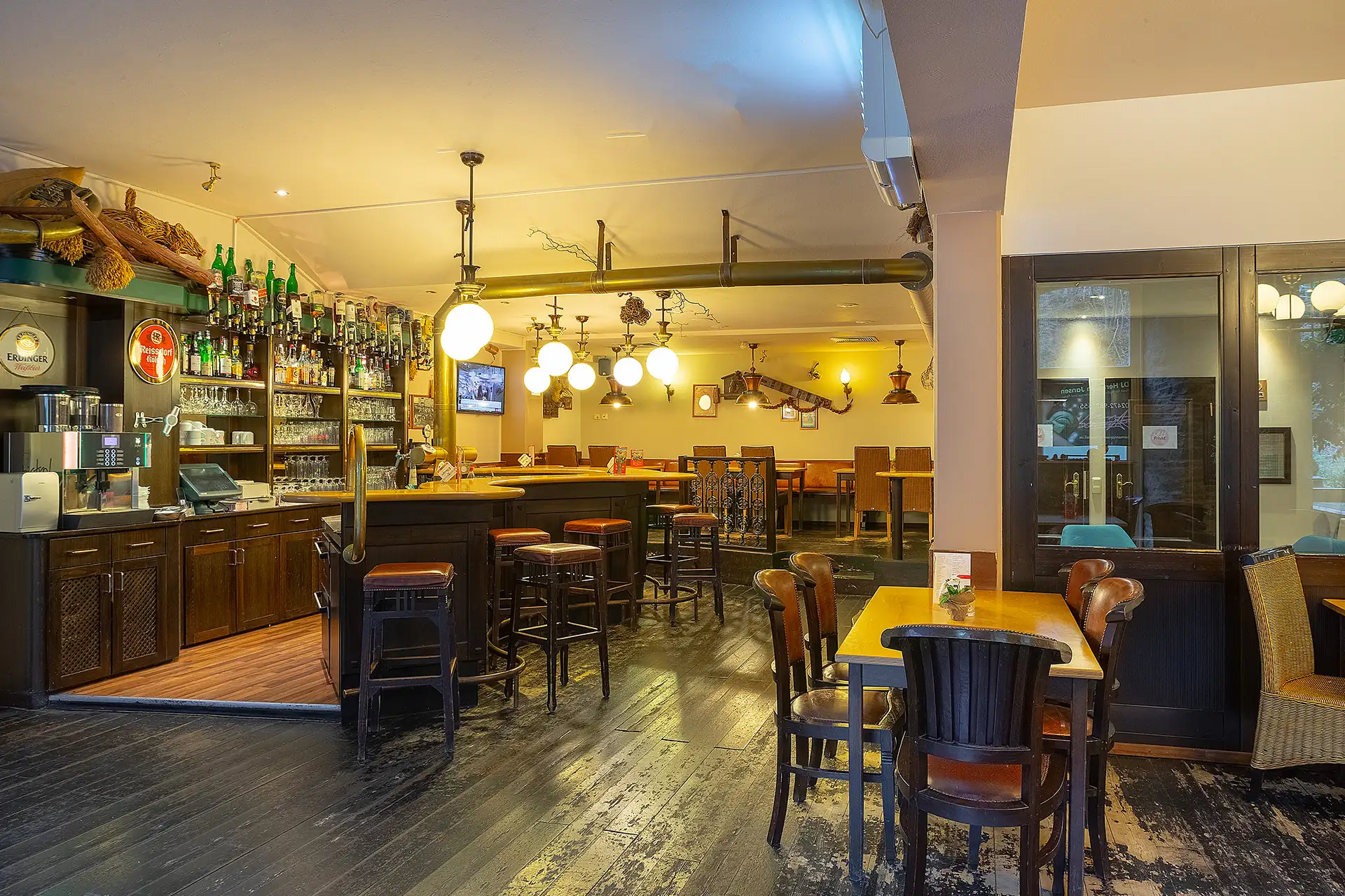 Gemütliche Hotelbar mit Holzmöbeln, Bartresen, Hockern und mehreren Tischen in warm beleuchtetem Raum