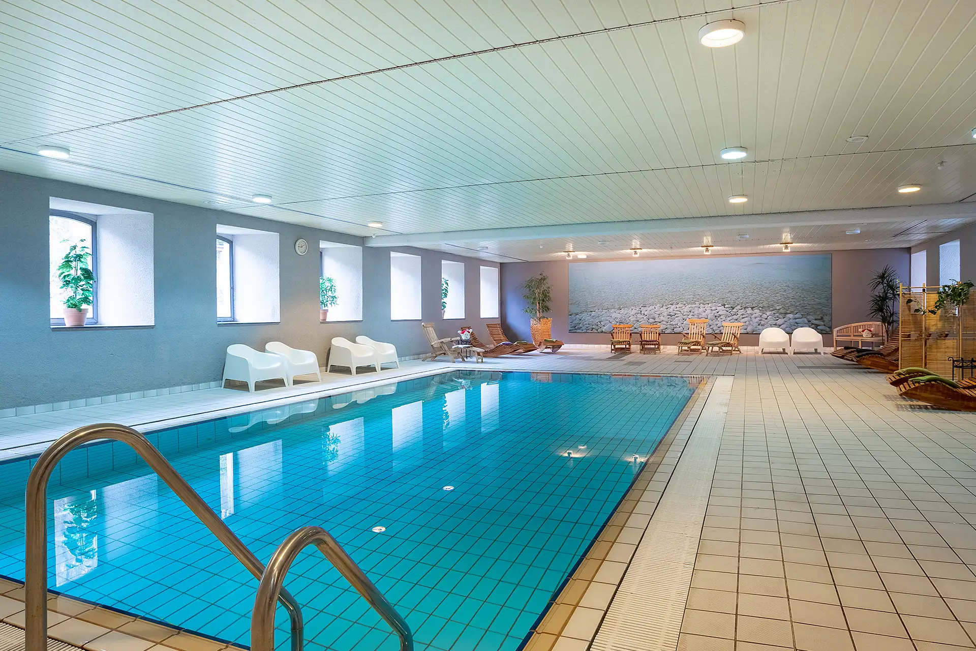 Wellnessbereich mit rechteckigem Schwimmbecken, Liegestühlen und großen Fenstern