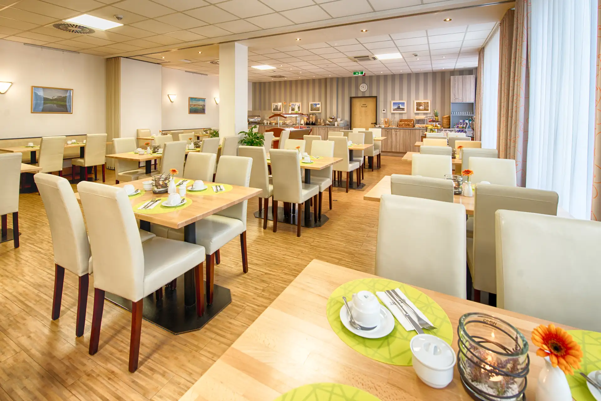 Frühstücksrestaurant im Achat Hotel Leipzig Messe: gedeckte Tischreihen und aufgebautes Buffet im Hintergrund.
