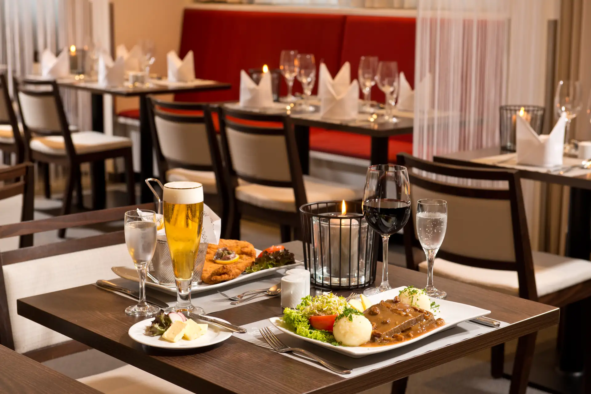 Abendessen im Achat Premium Dresden Elbufer: gedeckter Tisch mit zwei herzhaften Speisen, Wasser, Wein und Bier.