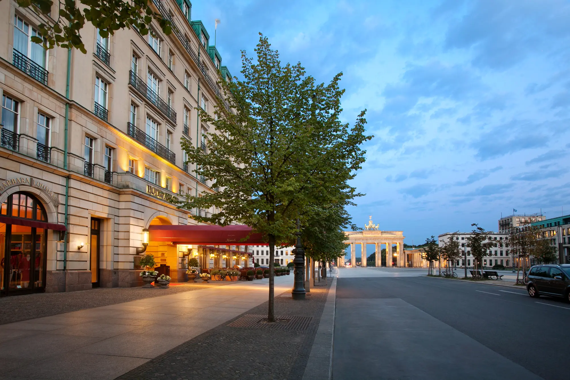 seitlicher Blick auf die Außenansicht vom Hotel Adlon Kempinski Berlin und dem Brandenburger Tor in der Abenddämmerung