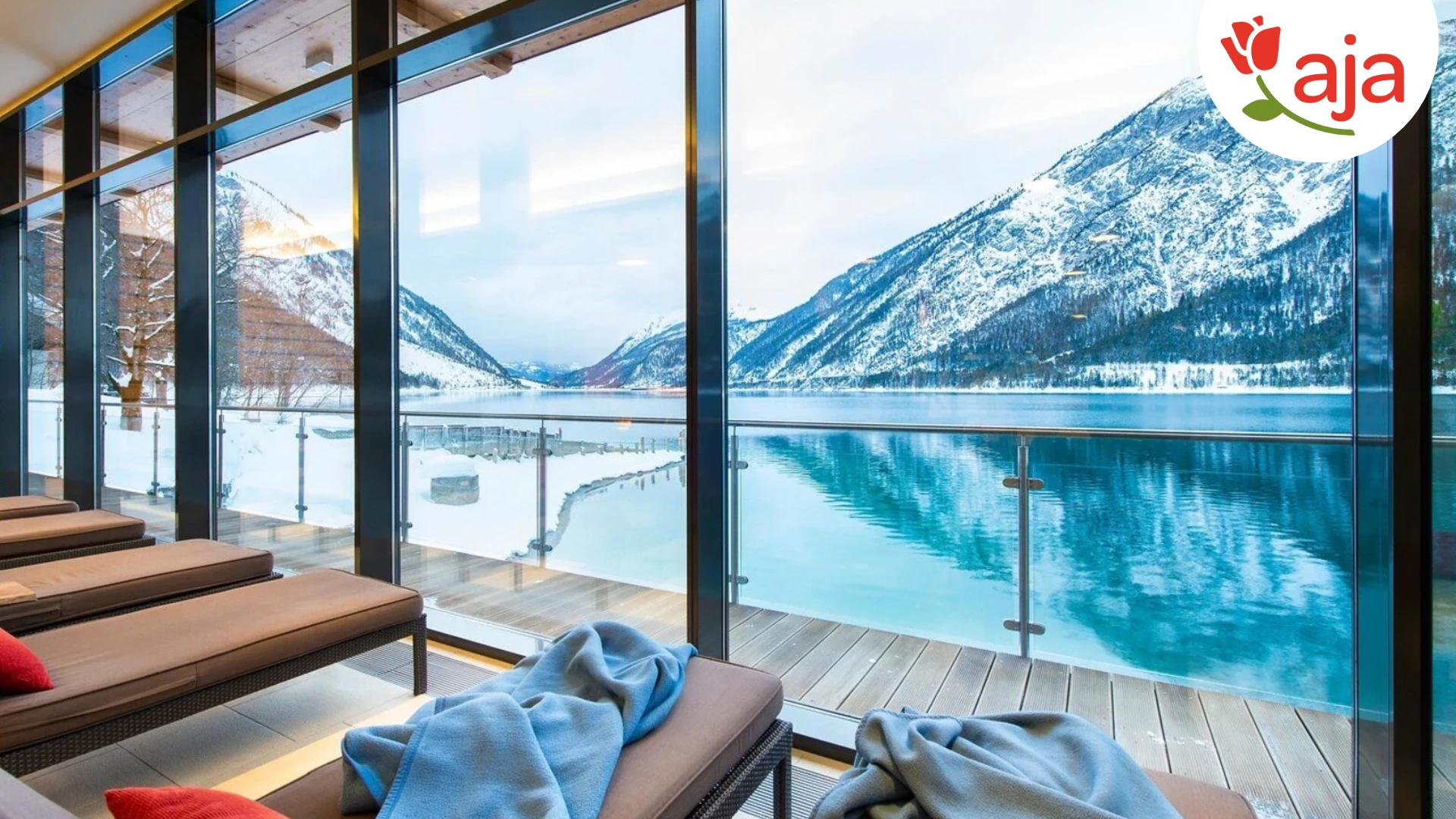 Blick aus dem Wellnessbereich im aja Fürstenhaus am Achensee auf den Achensee mit schneebedeckten Bergen im Hintergrund - mit Logo