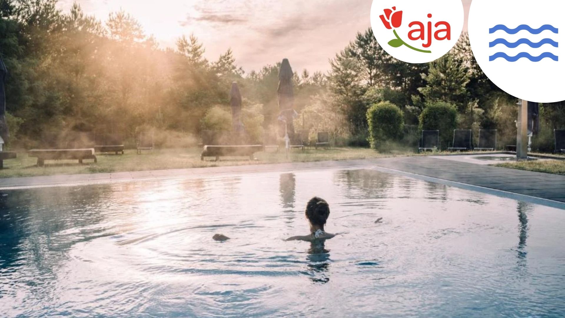 Ein idyllischer Außenpool im aja Resort Bad Saarow: Umgeben von grüner Natur und blauen Sonnenschirmen lädt der Pool mit glitzerndem Wasser zu einem entspannten Start in den Tag ein. Die sanften Sonnenstrahlen am Morgen sorgen für eine ruhige und erfrischende Atmosphäre. -mit Logo und Wellen-Icon