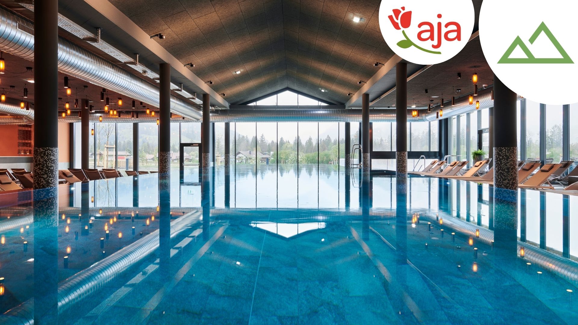 aja Ruhpolding, Blick auf die Wasserfläche des Innenpools mit Liegen an beiden Seiten -mit Logo und Berge-Icon