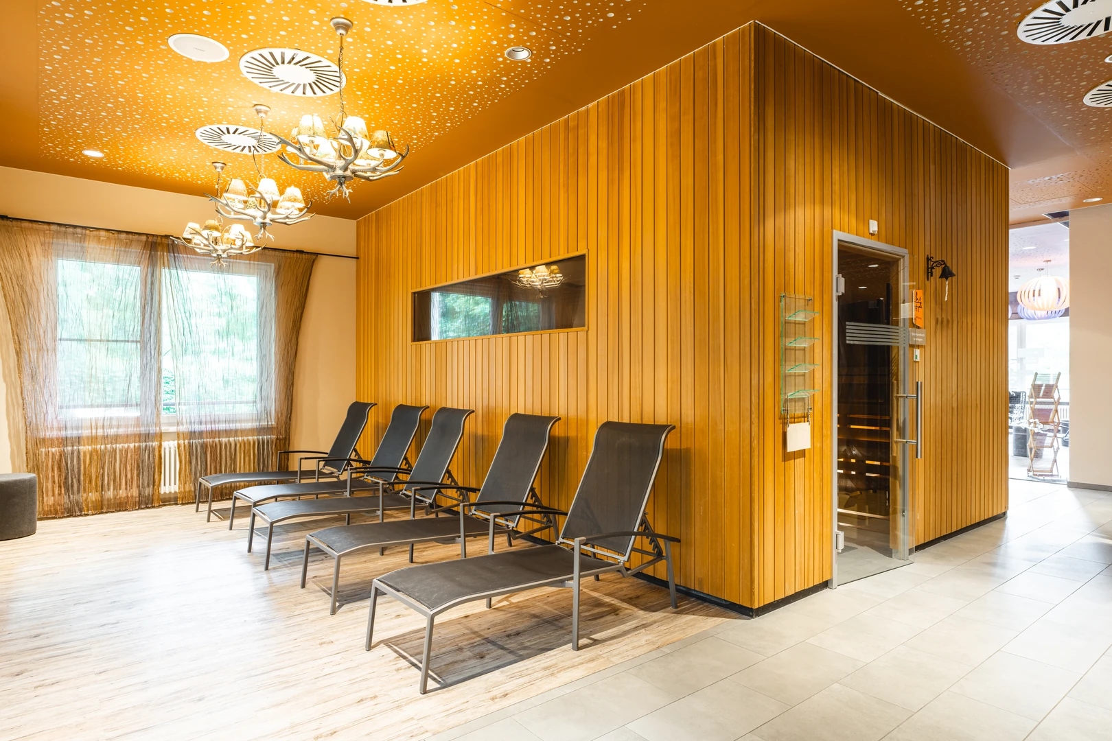 Der gemütliche Ruheraum im aja Resort Bad Saarow lädt mit seiner warmen Holzverkleidung und stilvollen Liegen zur vollkommenen Entspannung ein. Dezente Beleuchtung und moderne Gestaltung schaffen eine ruhige Atmosphäre, ideal nach einem erholsamen Saunagang.