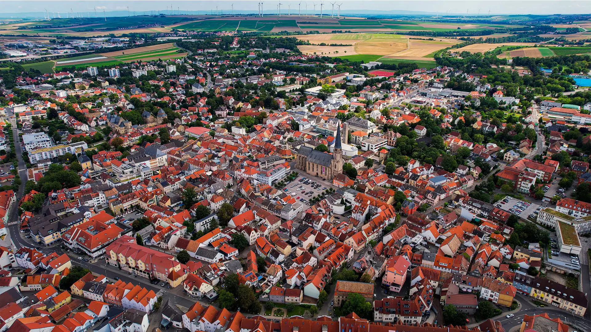 Luftaufnahme der Stadt Alzey mit dicht bebautem historischen Stadtkern, markanter Kirche mit Turm und umliegenden Feldern im Hintergrund