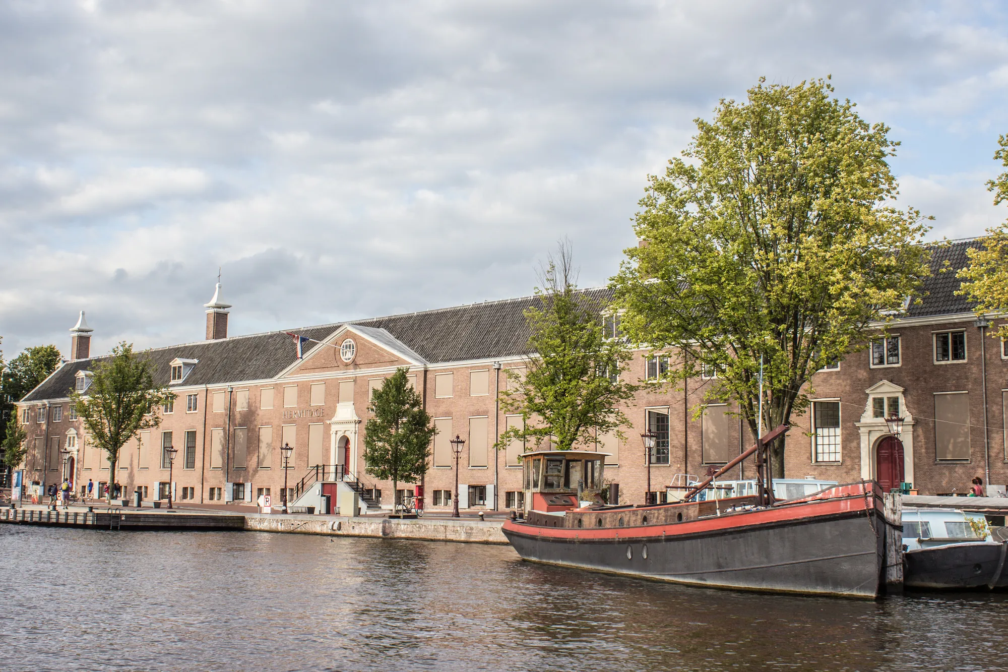 Die Hermitage Amsterdam am Grachtenufer, majestätisch in einem historischen Gebäude, umgeben von sanften Wasserflächen und hübschen Uferlandschaften, strahlt kulturelle Bedeutung und architektonische Eleganz aus.