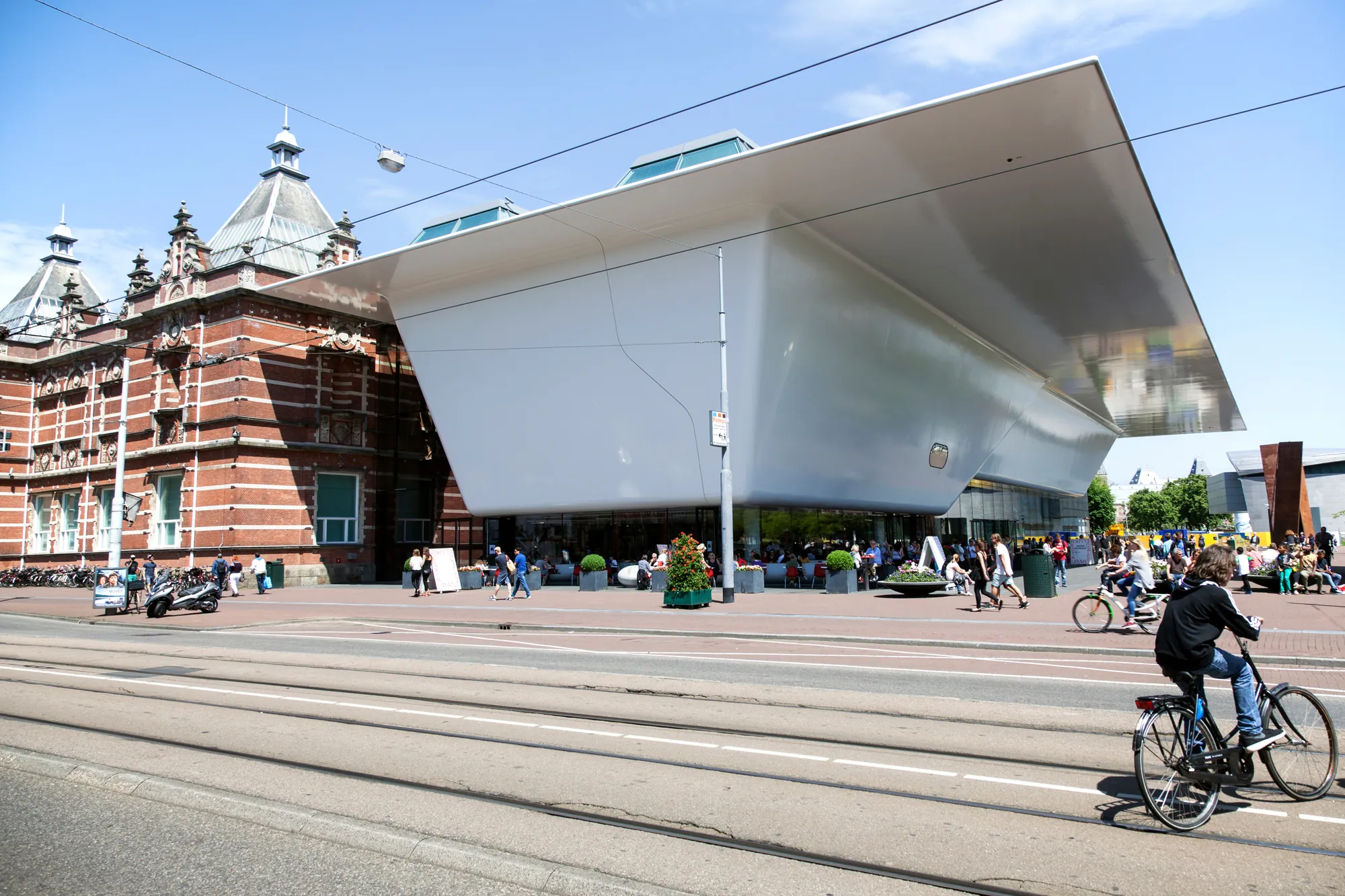 Außenansicht des Stedelijk Museums in Amsterdam an einem hellen Tag, die moderne Architektur des Gebäudes strahlt im Sonnenlicht und zieht die Aufmerksamkeit der Passanten auf sich.