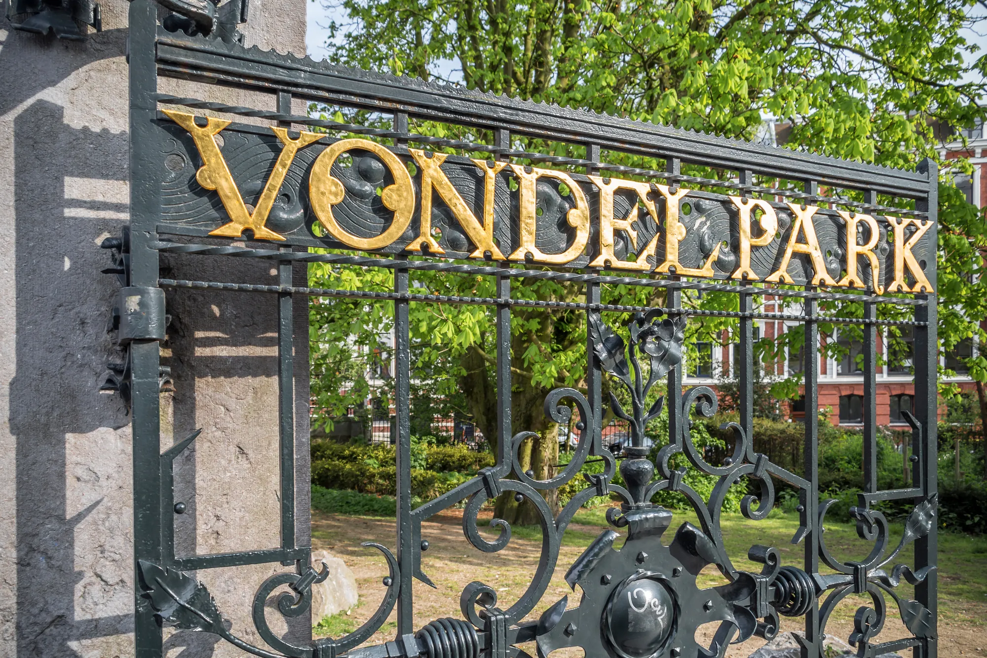 Nahaufnahme des Eingangs zum Vondelpark mit kunstvoller, goldverzierter Schrift, die die Pracht des Parks hervorhebt.