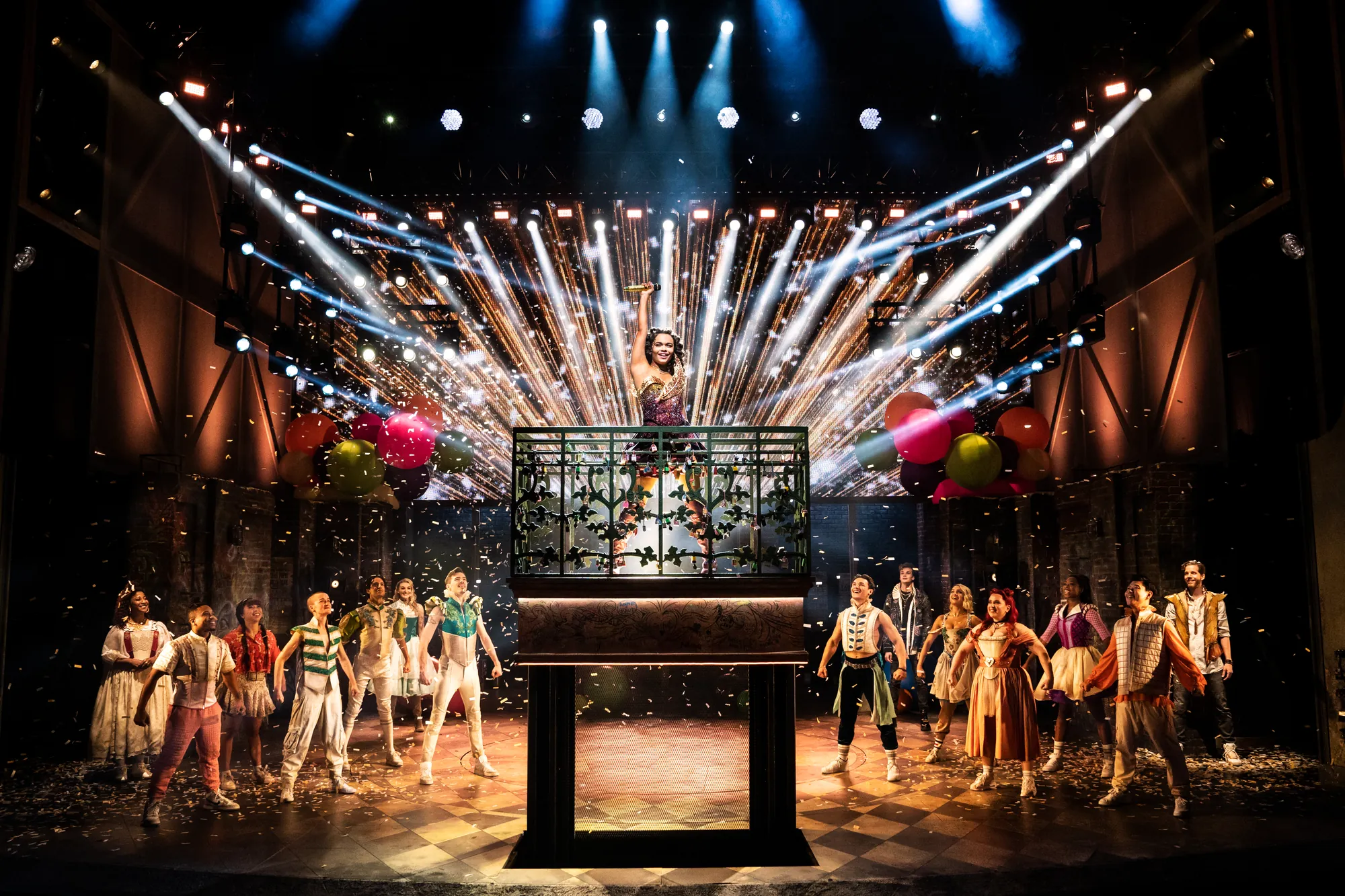 Eine lebhafte Broadway-Szene mit Darstellern in farbenfrohen Kostümen, die auf der Bühne mit dynamischer Beleuchtung und feierlichen Luftballons auftreten.